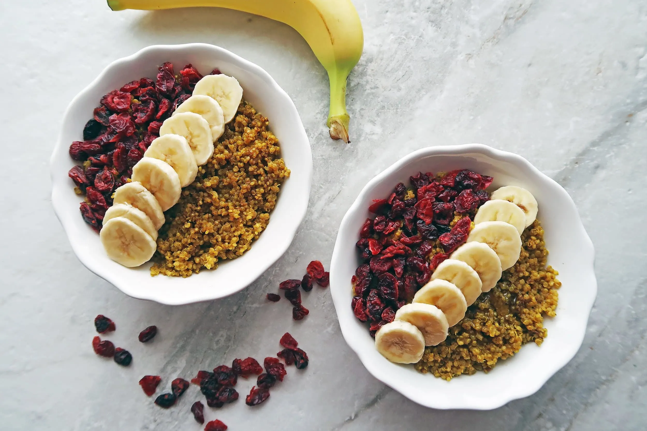 Two golden milk (turmeric latte) quinoa bowls garnished with dried cranberries and banana slices.