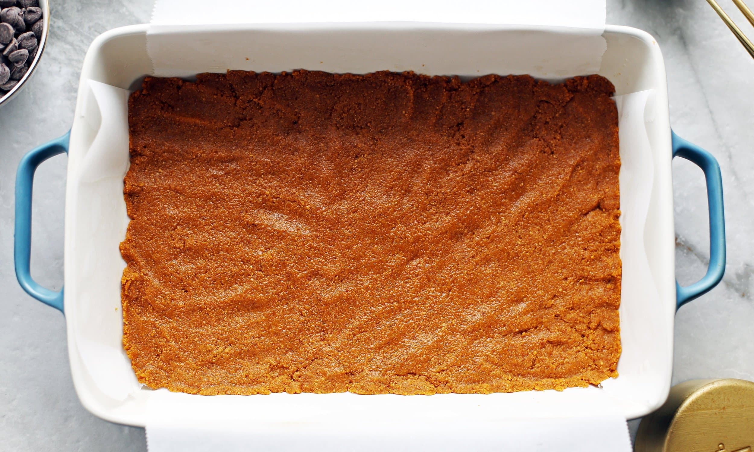 Combined graham cracker crumbs and melted butter pressed into an even layer into a baking dish lined with parchment paper.