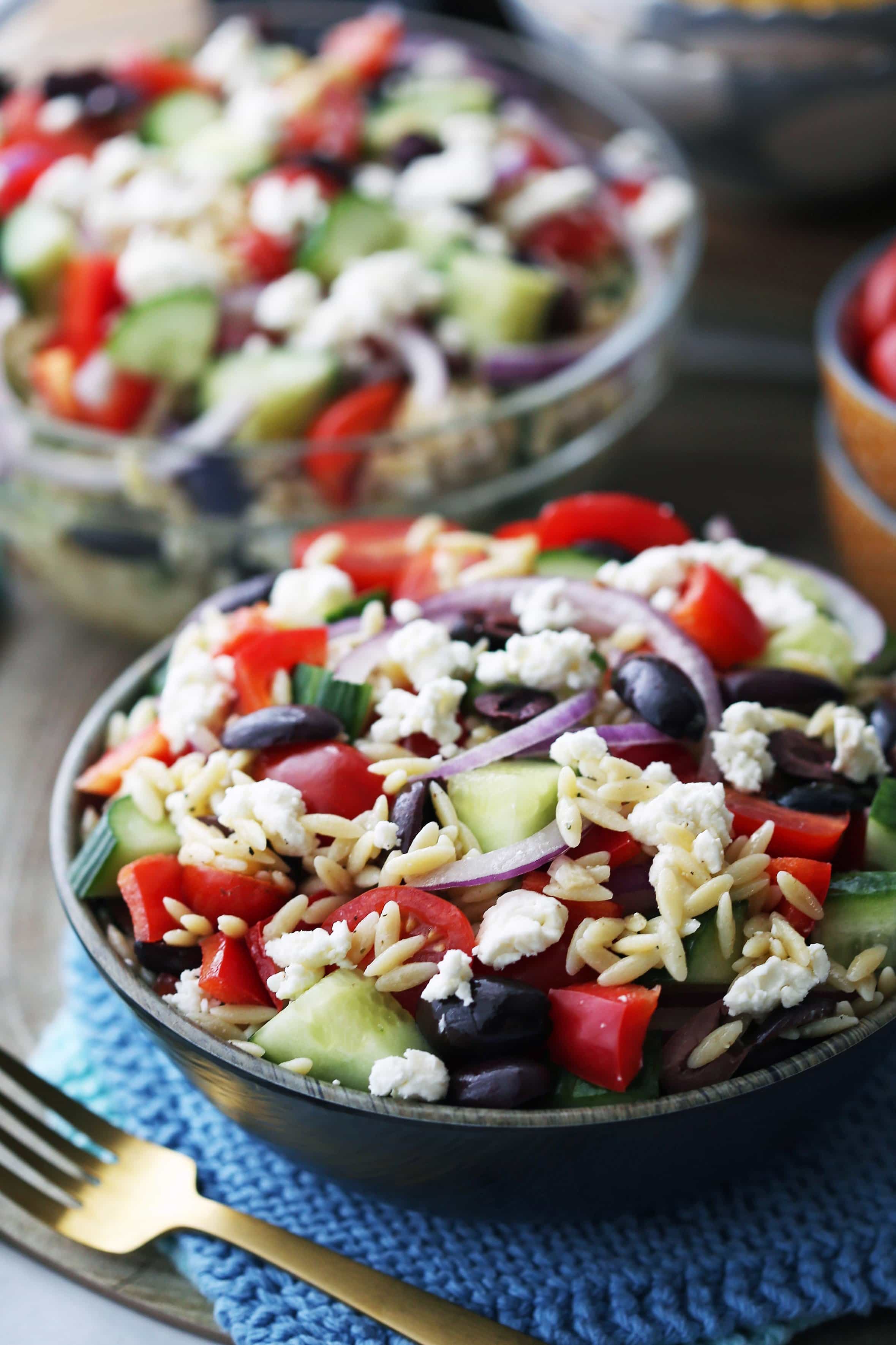 Greek orzo pasta salad with lemon vinaigrette in a brown bowl and in a large glass bowl.