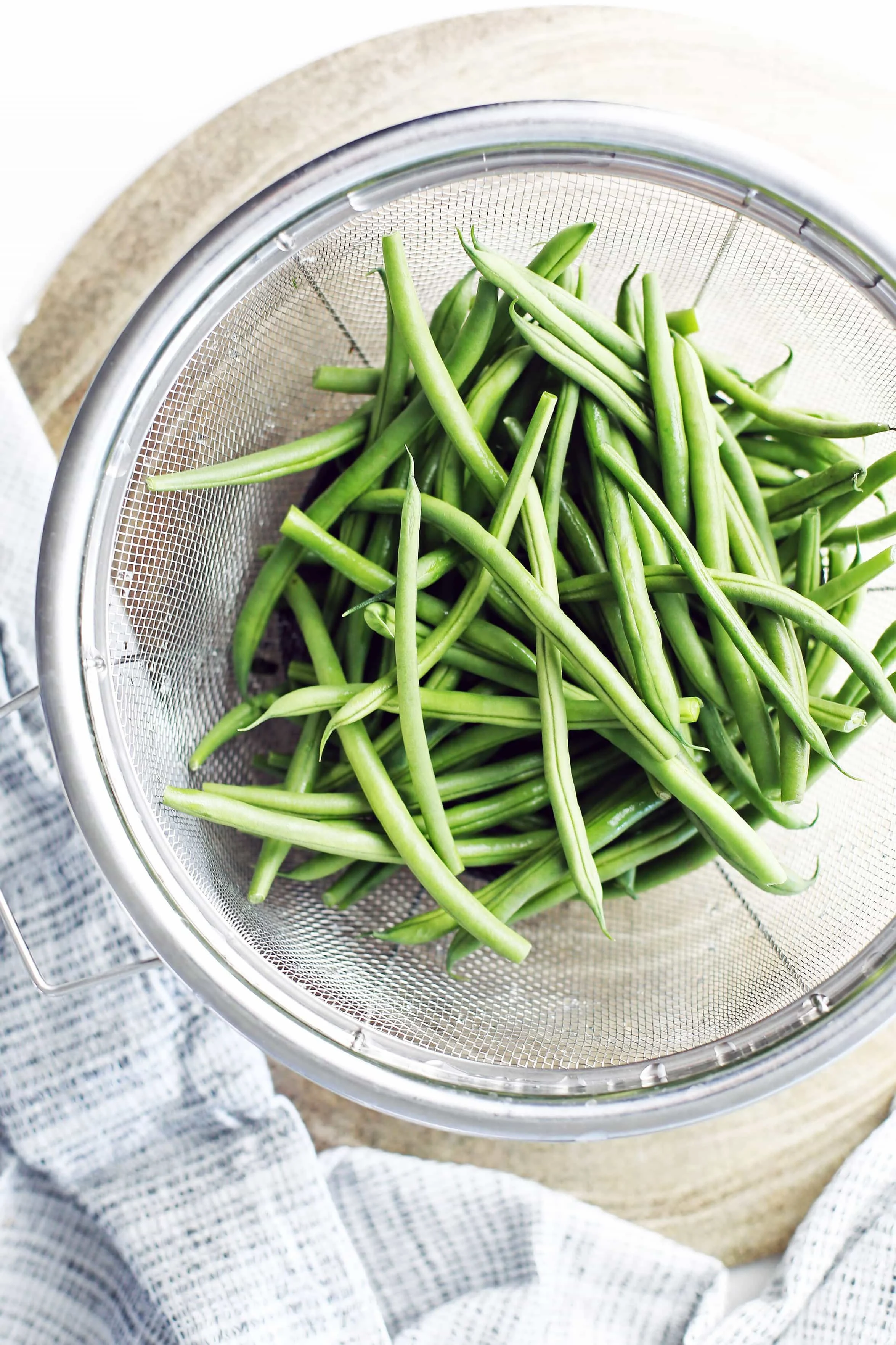Overhead view of rinsed and trimmed French green beans in large metal mesh strainer.