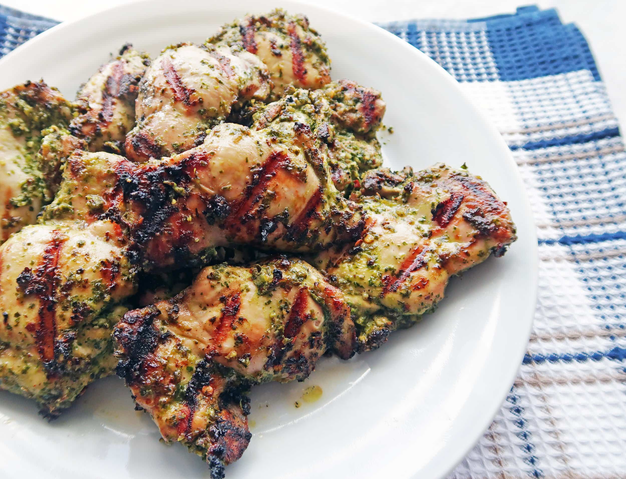 Side angled view of a white plate Grilled Chicken Thighs with Chimichurri Sauce on top of a blue checkered towel.