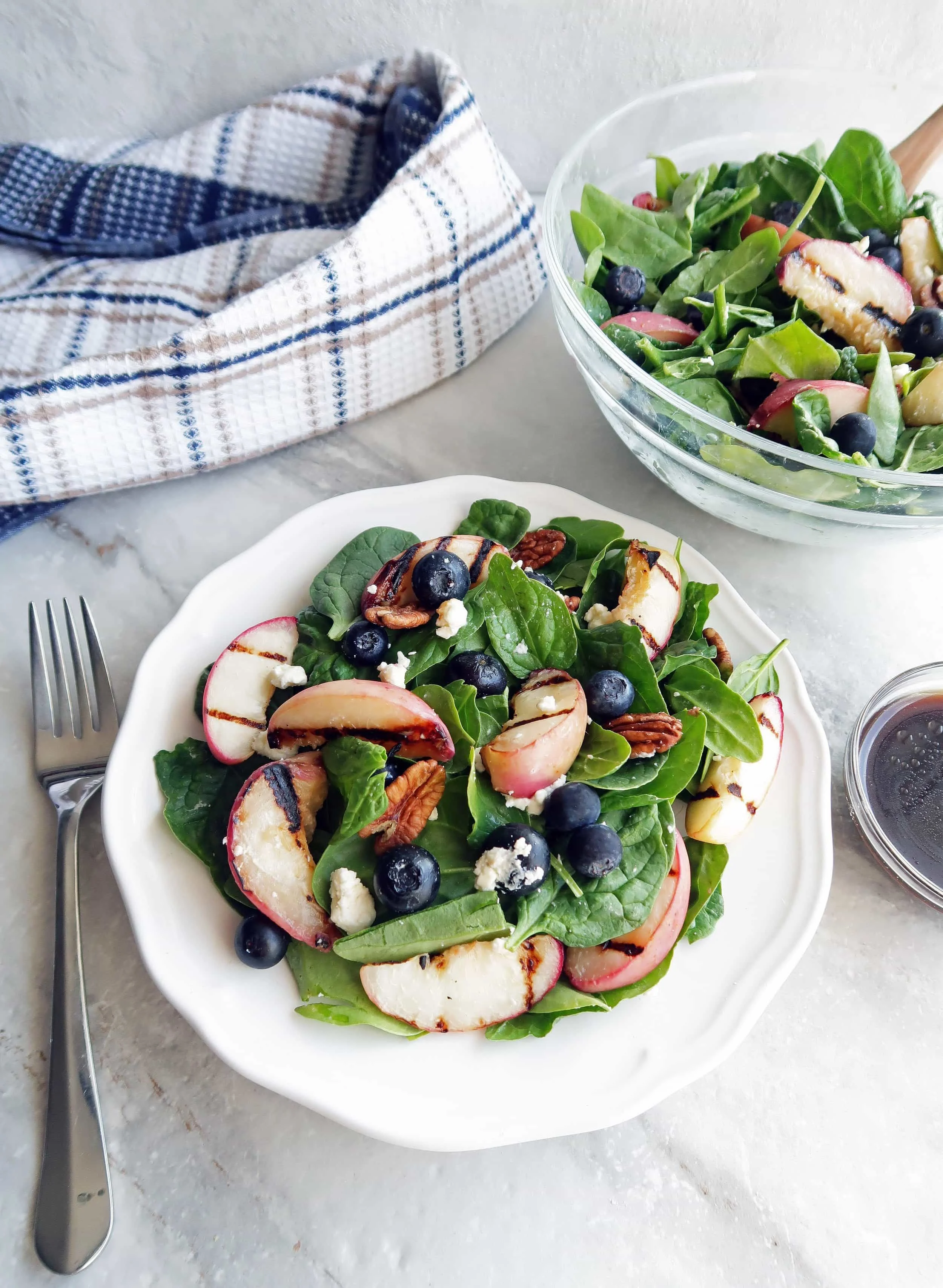 A plate of Grilled Peach Blueberry Spinach Salad with more salad and honey balsamic vinaigrette to the side.