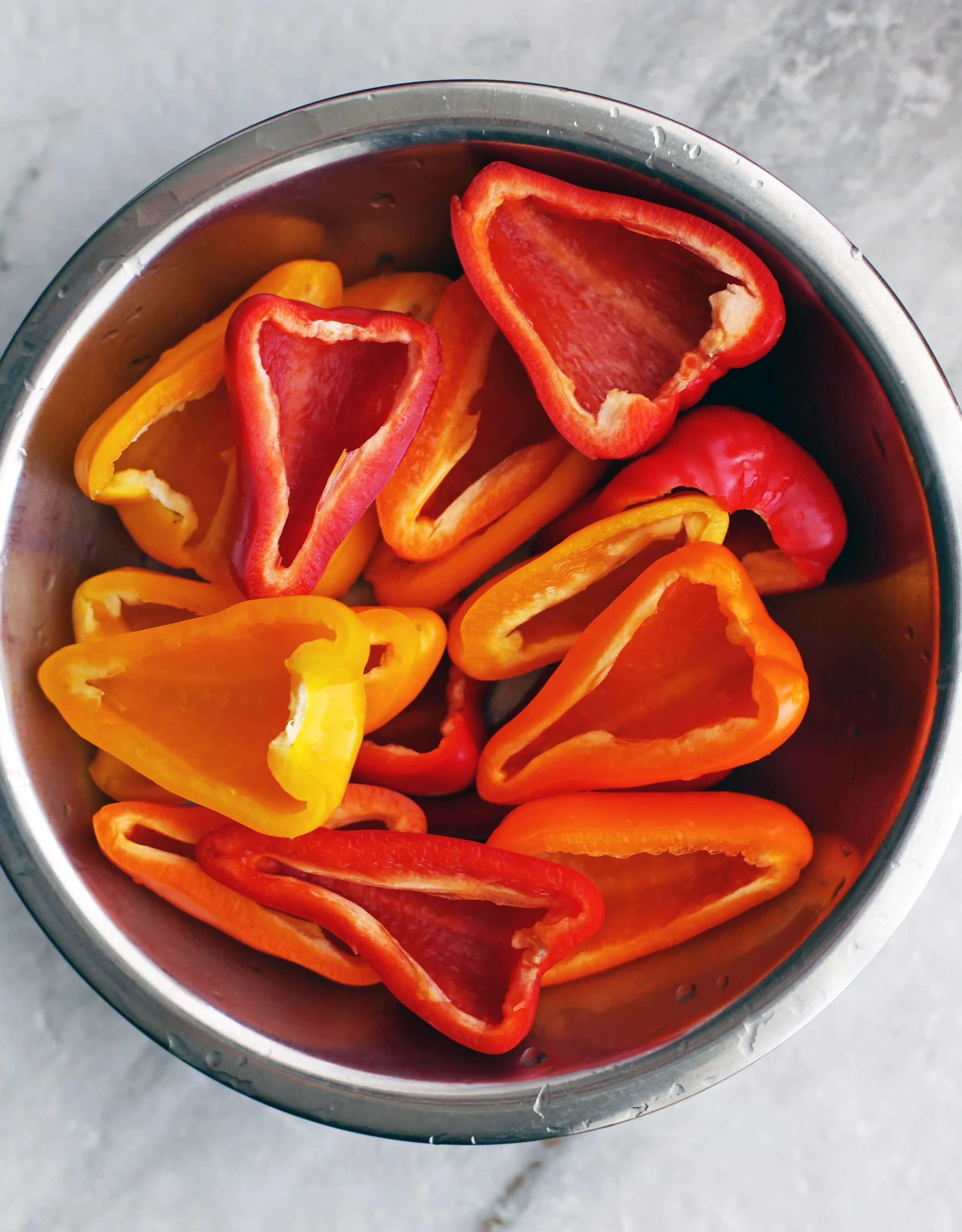 A metal bowl containing baby bell peppers that are sliced lengthwise and seeded.