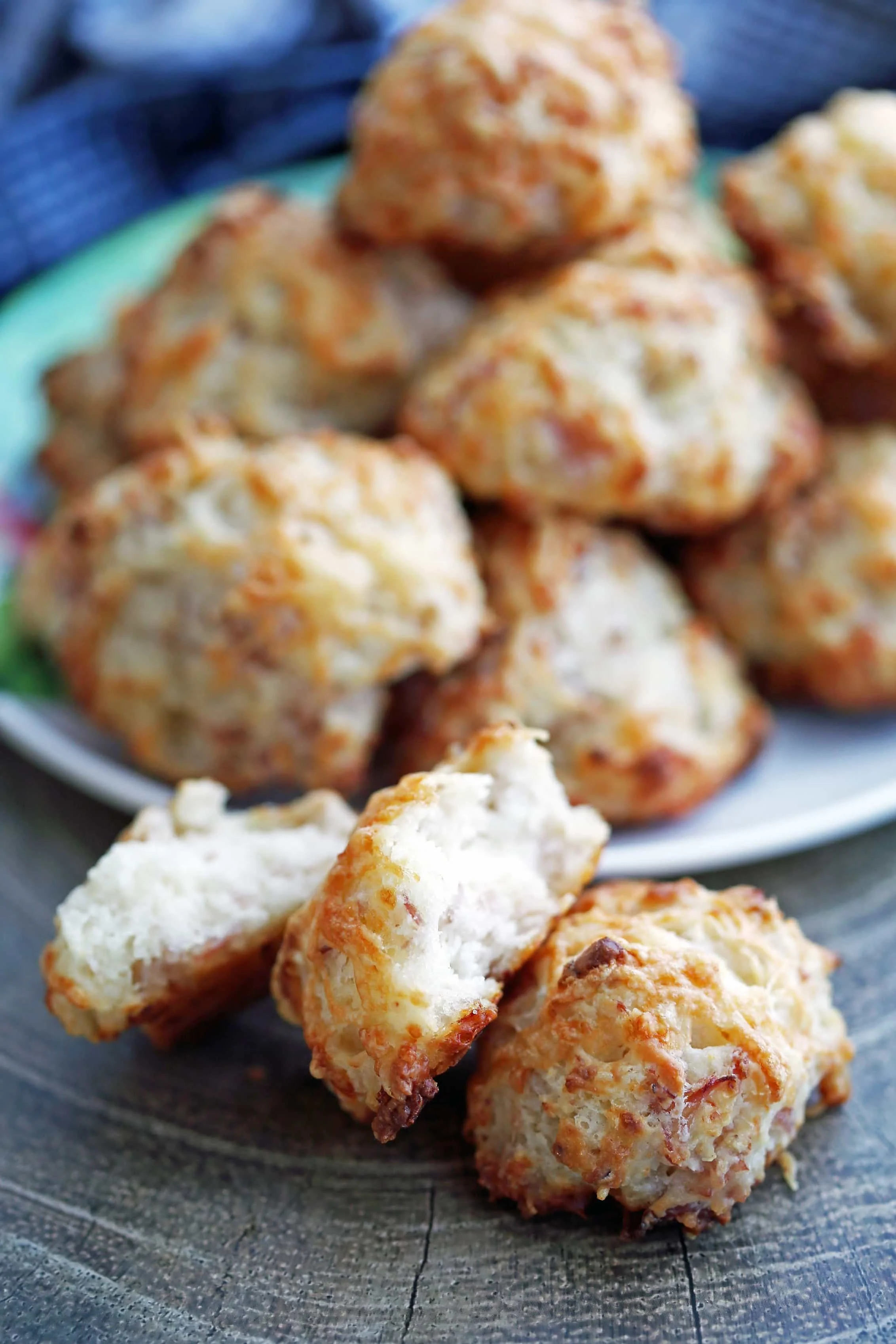 Two ham and cheese drop biscuits, one broken in half, on a wooden platter with more drop biscuits behind them.