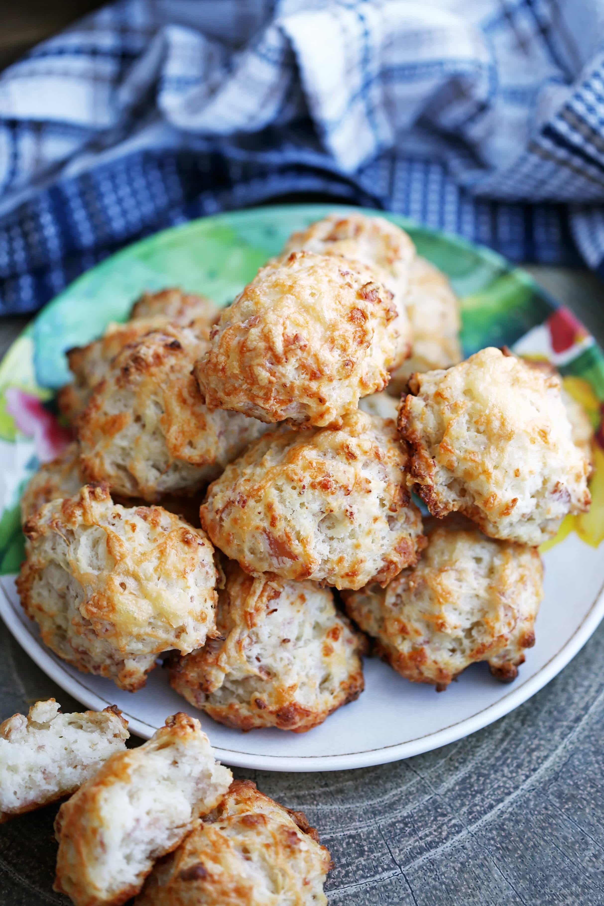A plate full of freshly baked ham and cheese drop biscuits piled on top of one another.