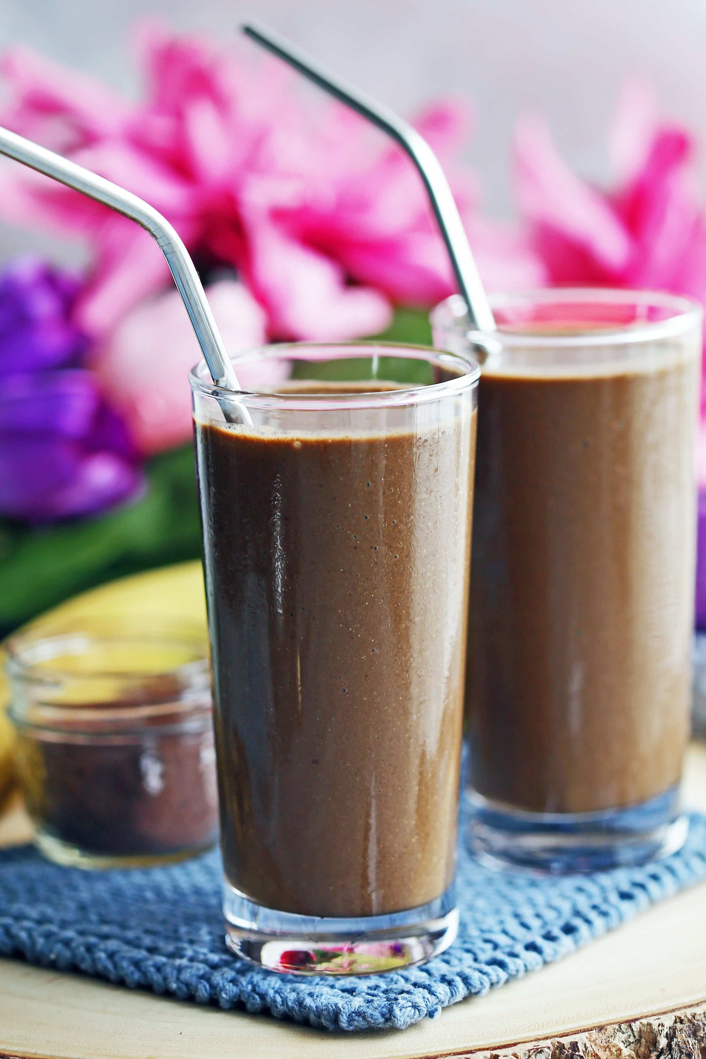 A side view of two tall glasses filled with chocolate banana smoothies on a blue knitted cloth.