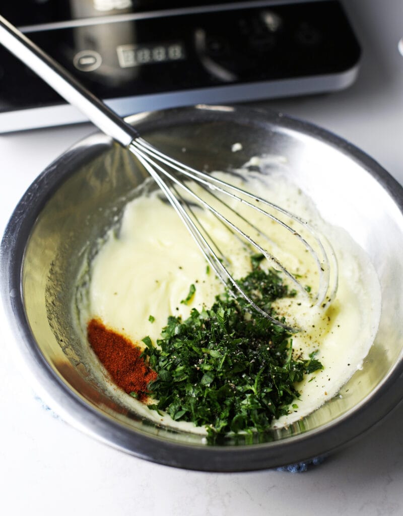 Hollandaise sauce with parsley, paprika, salt, and pepper in a stainless steel bowl.