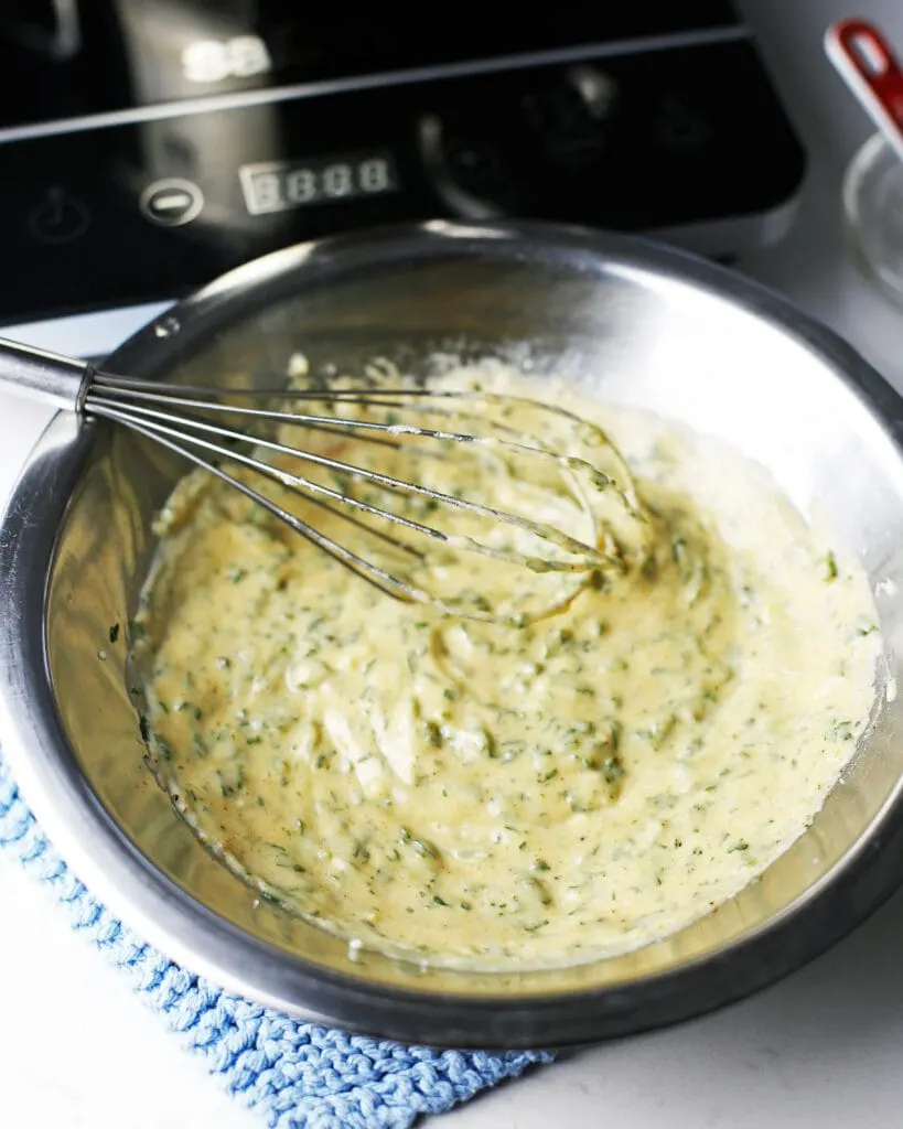 Parsley lemon hollandaise sauce and a wired whisk in a stainless steel mixing bowl.