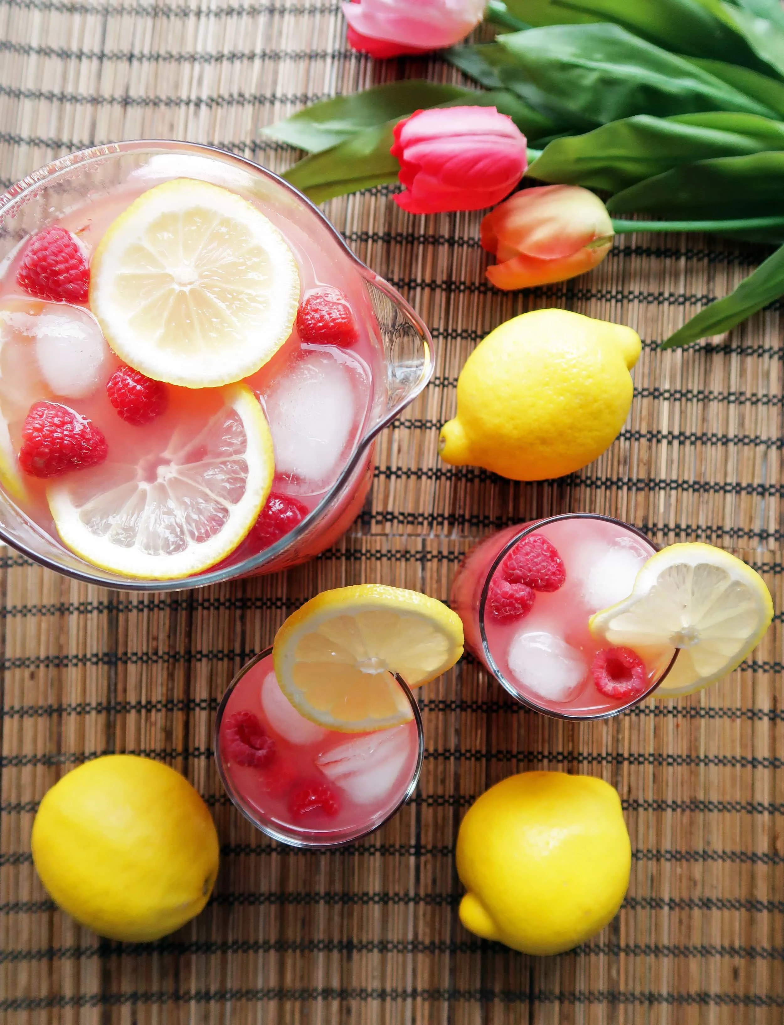 Two glasses and a pitcher full of homemade Raspberry Green Tea Lemonade with lemon slices and raspberry garnish