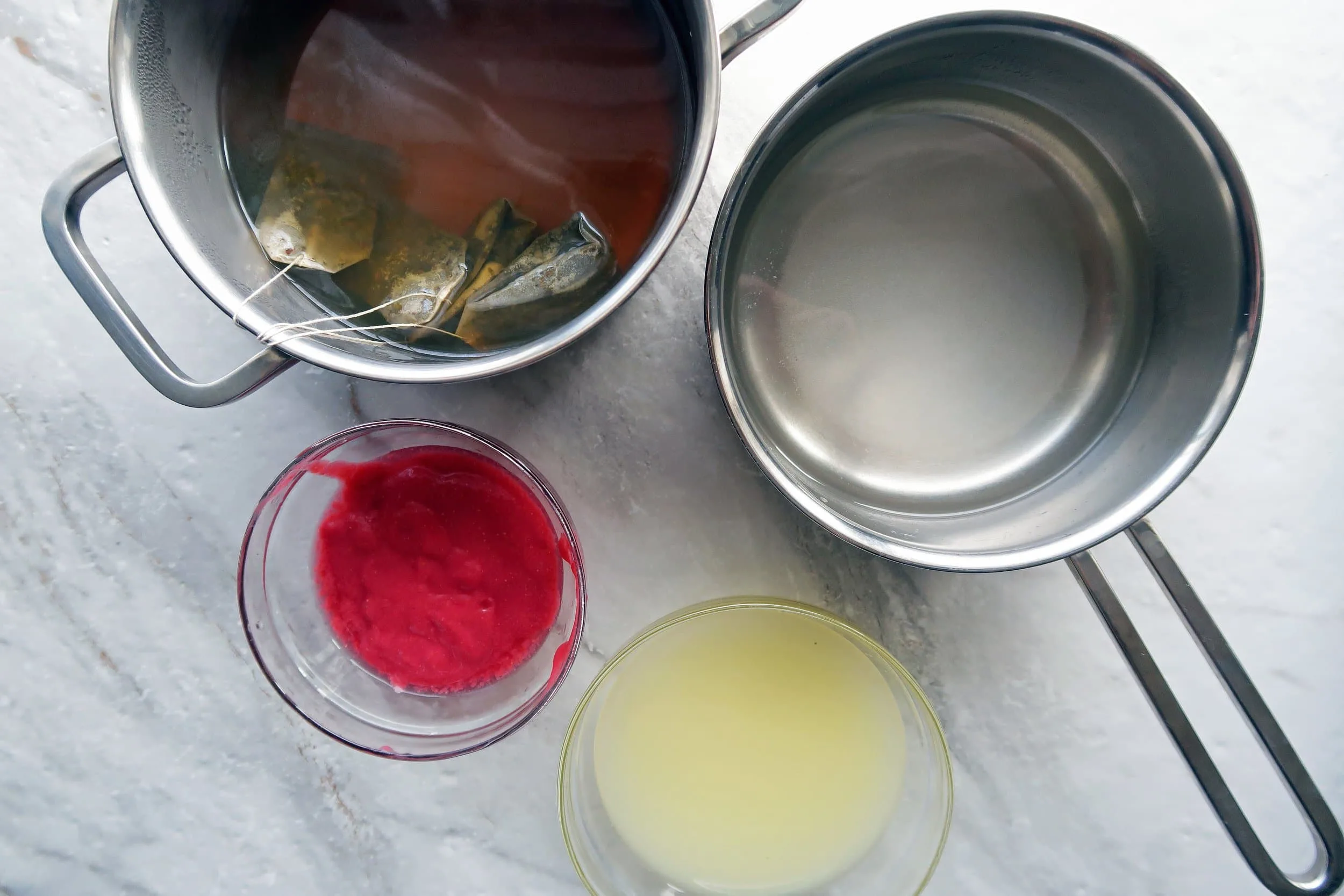 Pots of stepped green tea and simple syrup with bowls of lemon juice and raspberry puree.