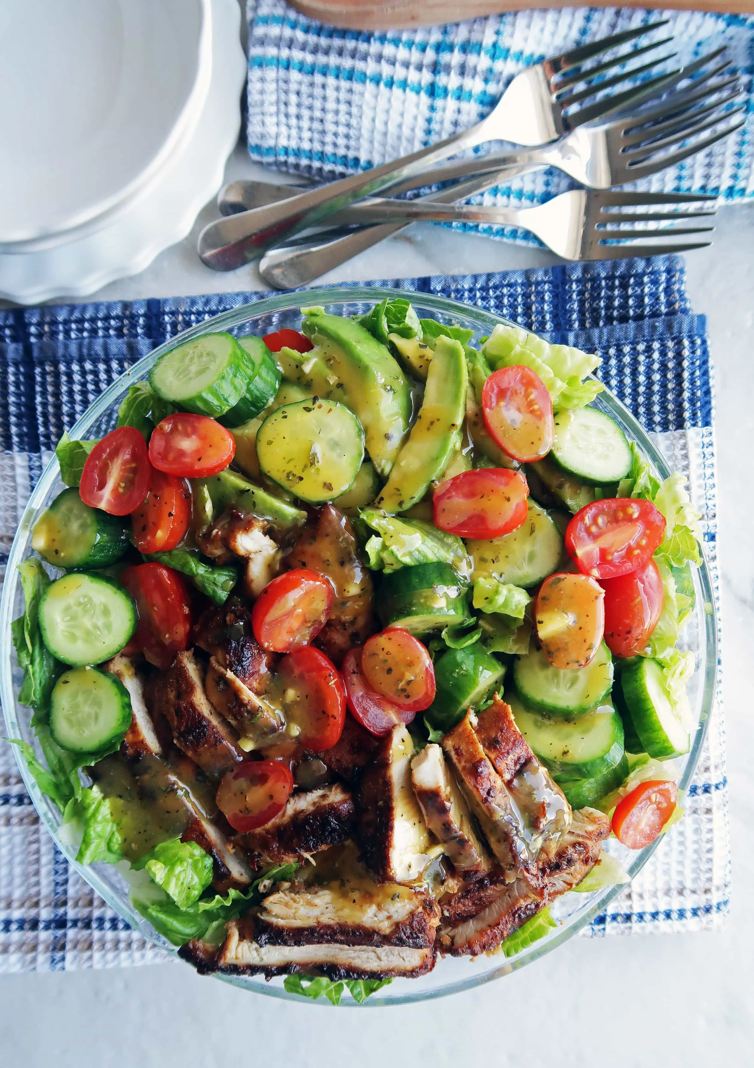 Romaine lettuce, cucumber, tomatoes, avocado, honey mustard chicken, and dressing in a large glass bowl.