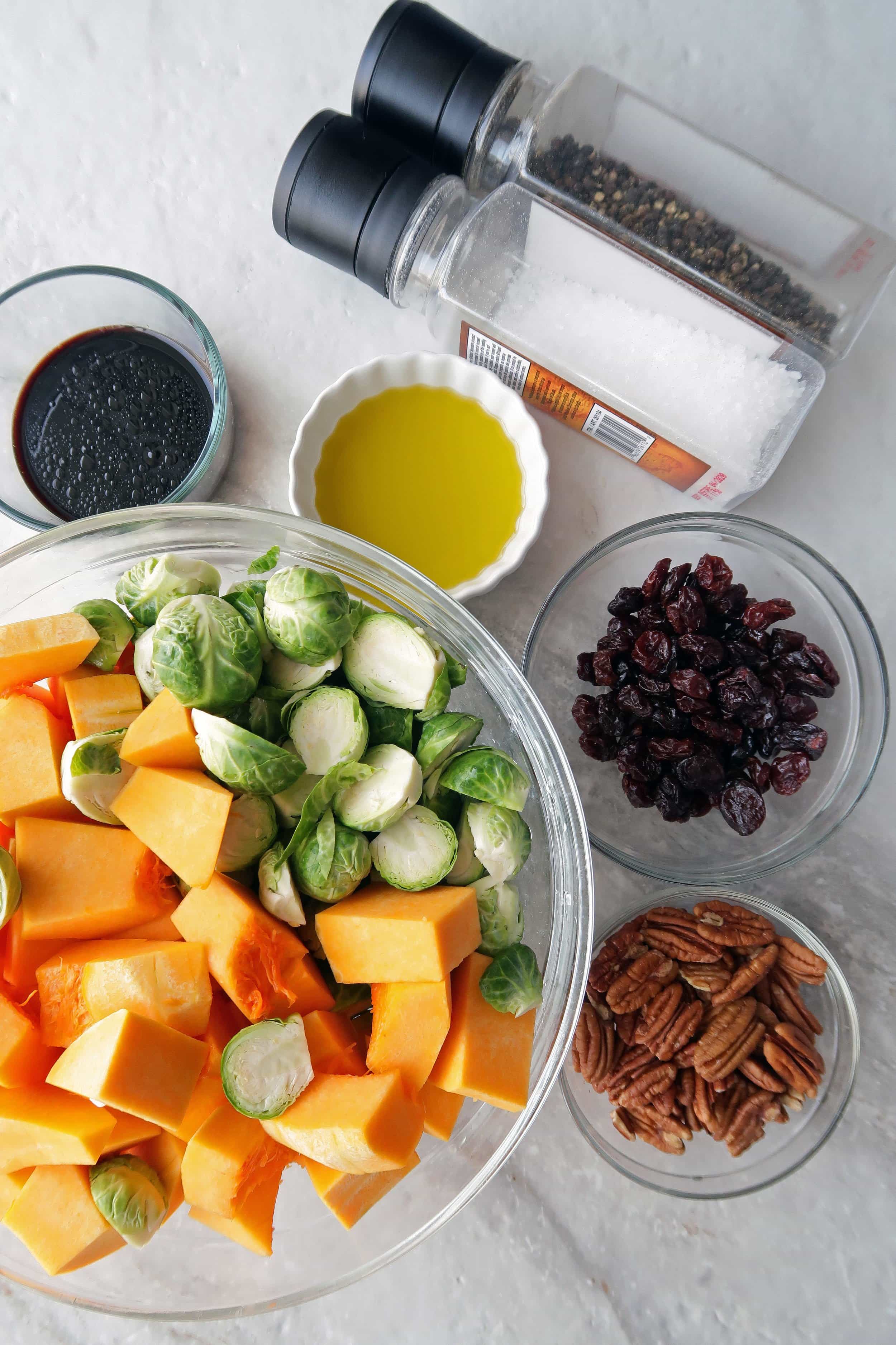 Chopped butternut squash, Brussels sprouts, pecans, dried cherries, balsamic vinegar, and oil in individual bowls.