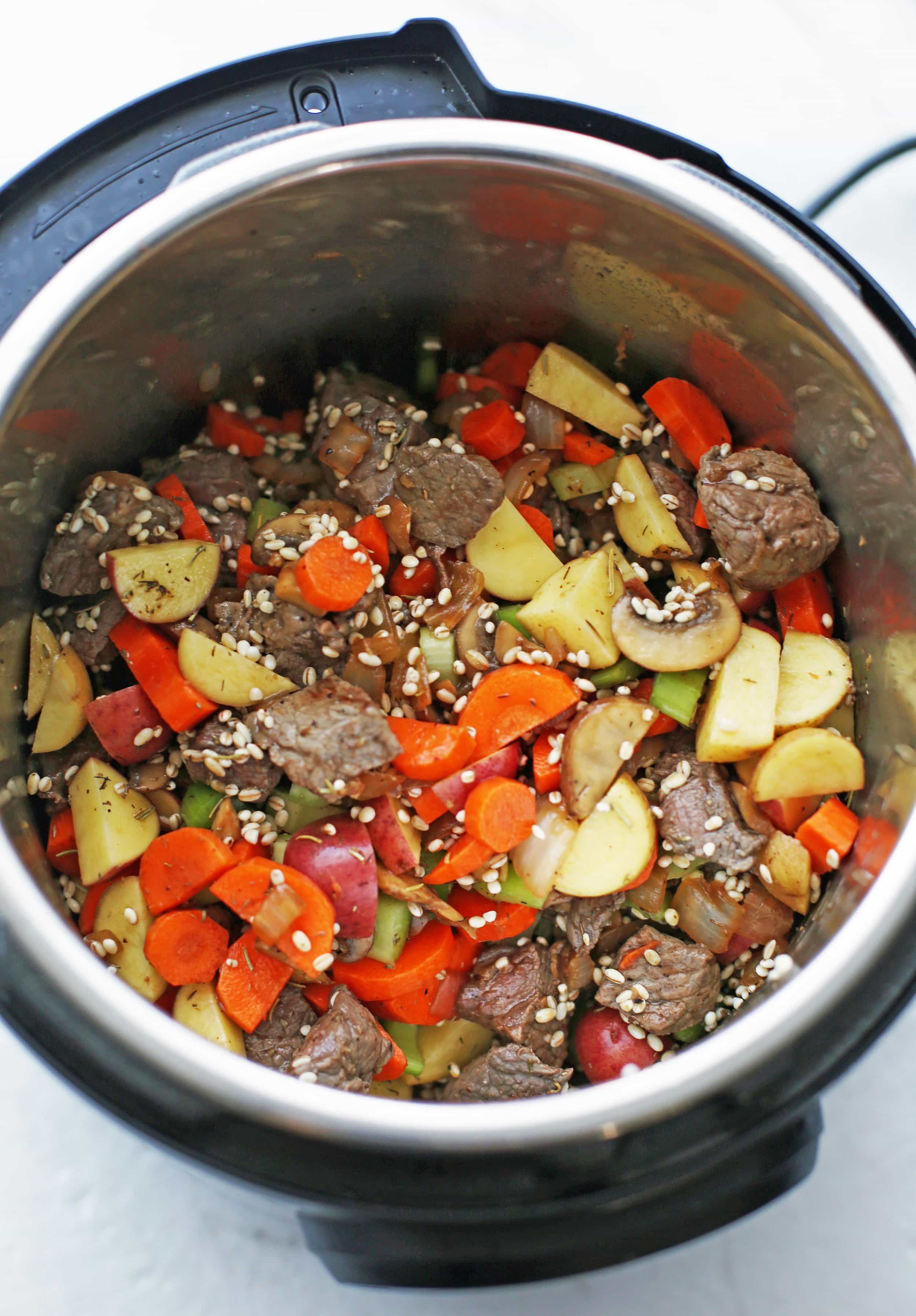 Browned beef, vegetables, dry pearl barley, and mushrooms stirred in the Instant Pot.