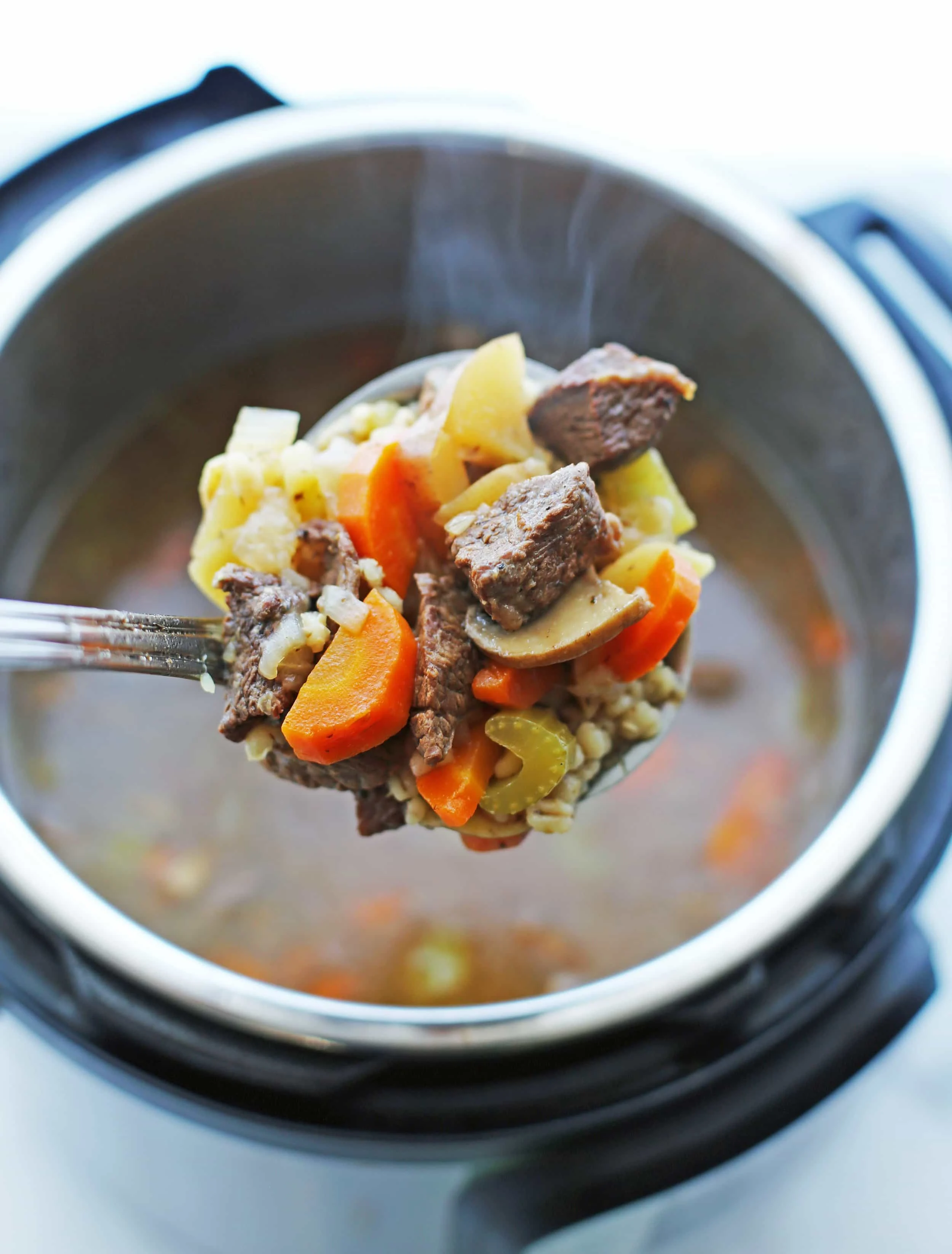 A close-up view of a ladle scoop of beef barley mushroom soup over the Instant Pot.