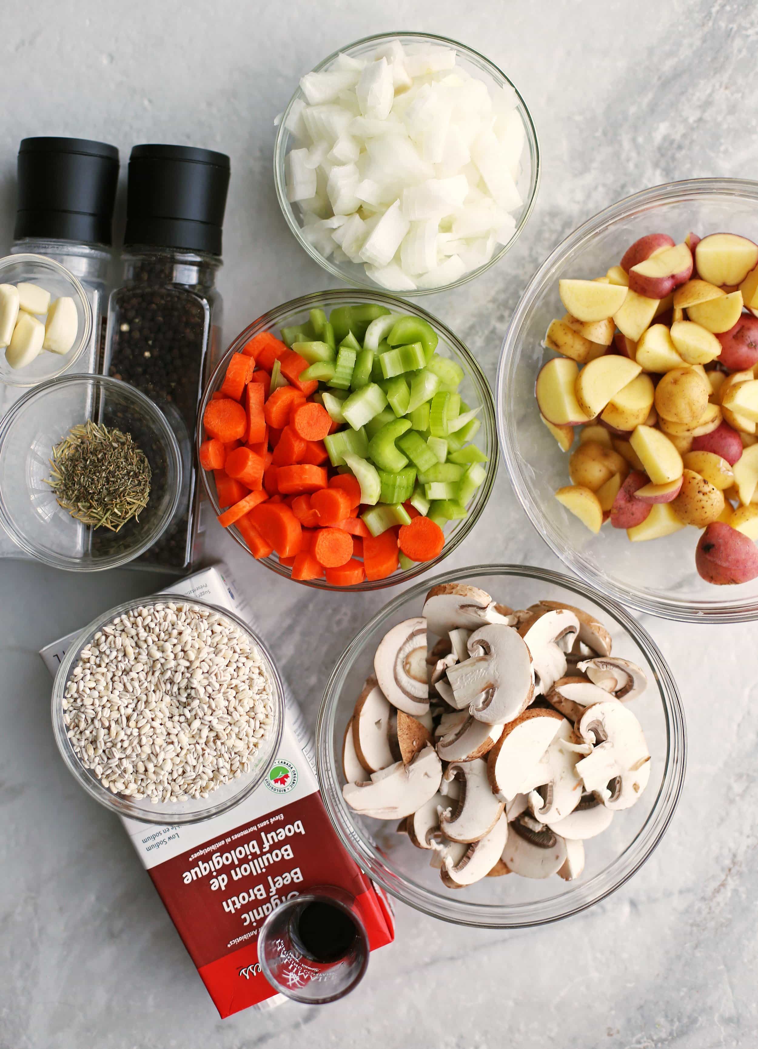 Bowls of sliced mushrooms, potatoes, celery, carrots, onions, pearl barley, garlic, and herbs.