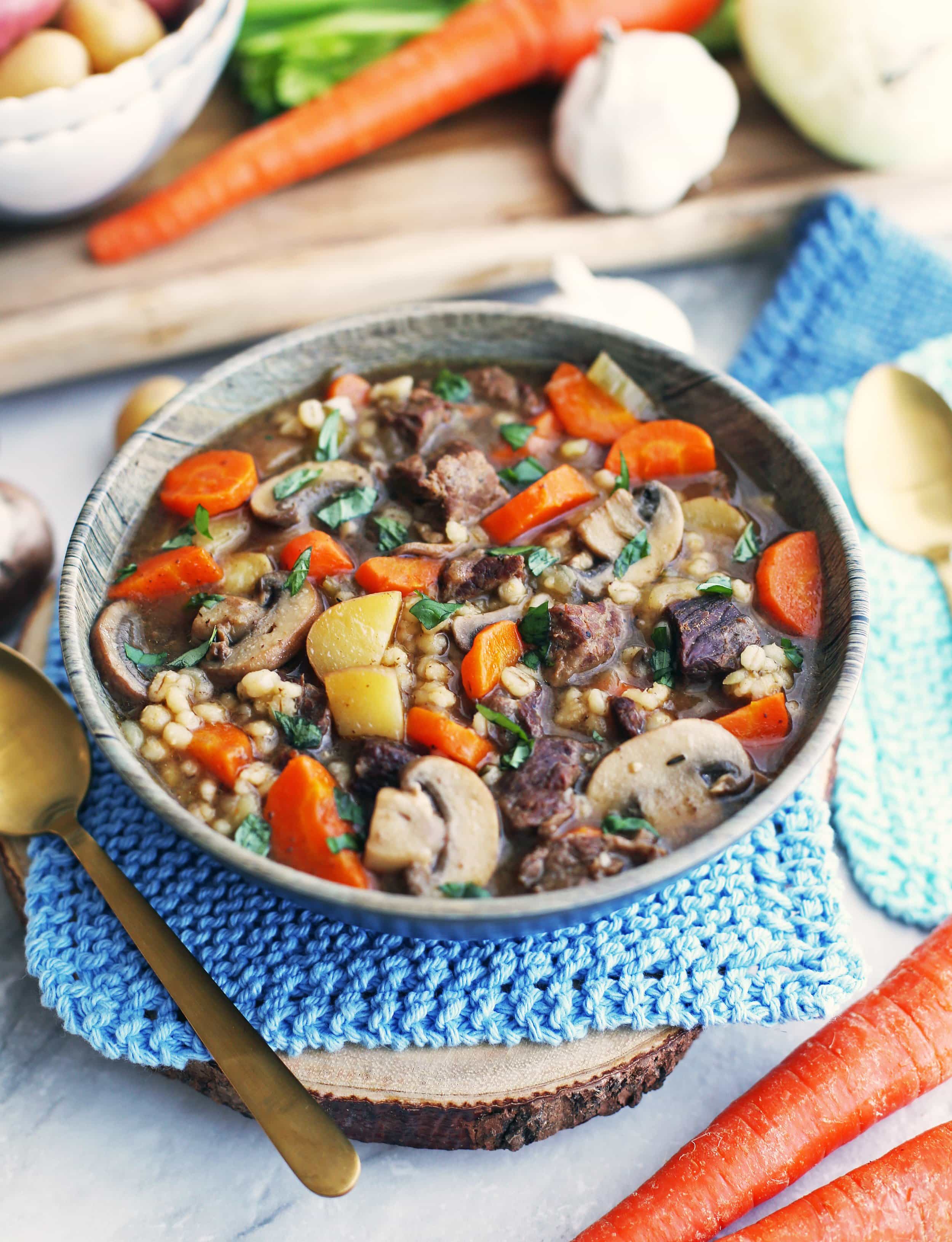 Top angled view of a bowl of beef barley mushroom soup with vegetables in a bowl.