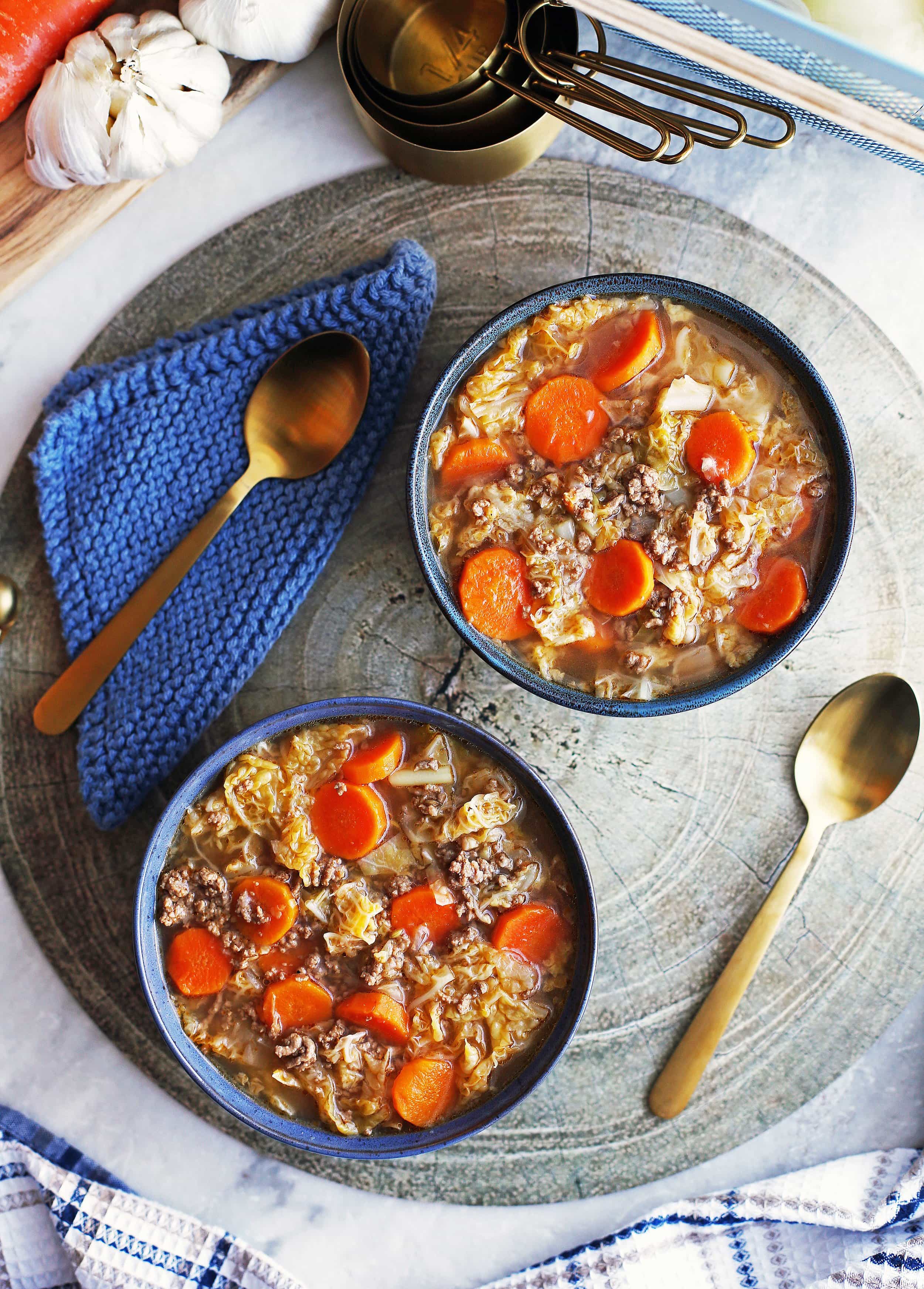 Overhead view of two blue bowls containing Beef and Cabbage Soup with spoons on the side.