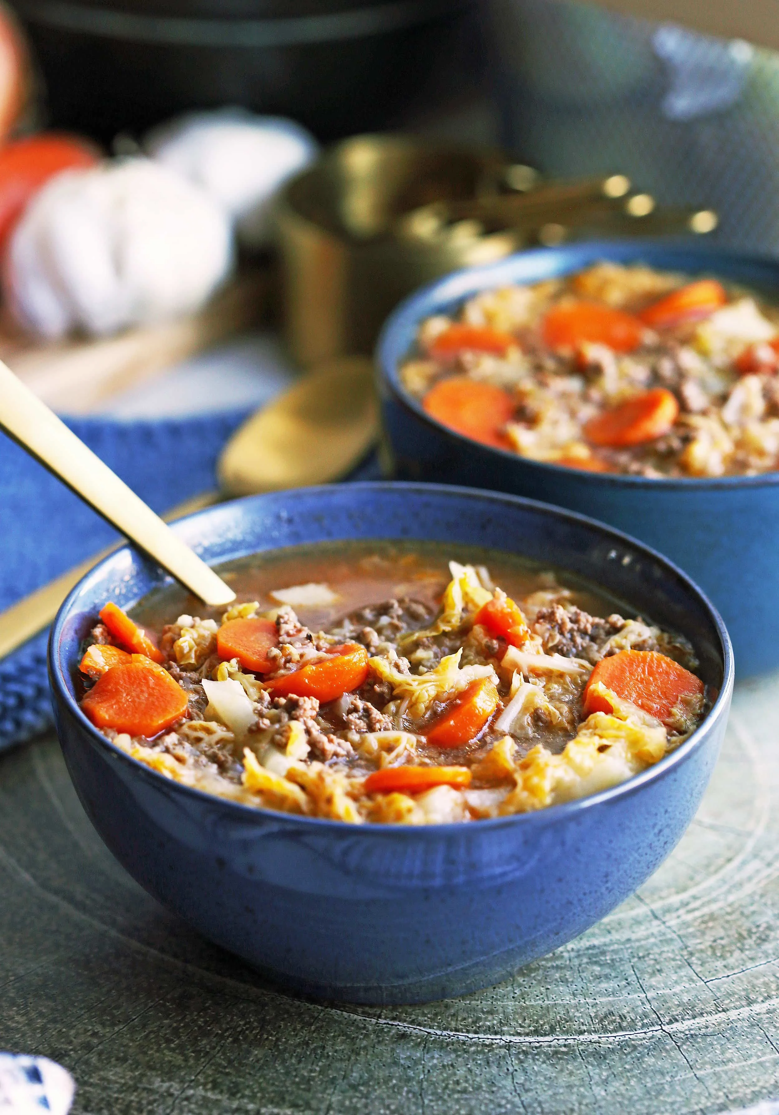 A closeup of Instant Pot Beef and Cabbage Soup in a blue bowl with a spoon in the soup.