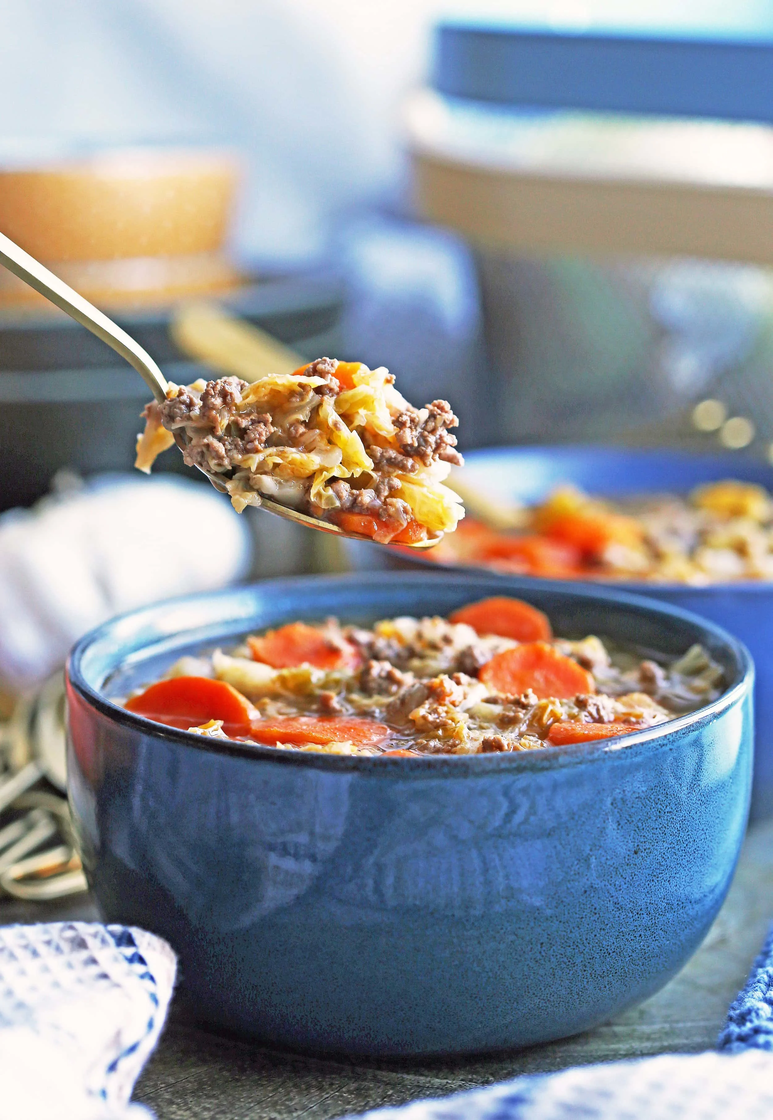 A big spoonful of Instant Pot Beef and Cabbage Soup over a blue bowl of the same soup.