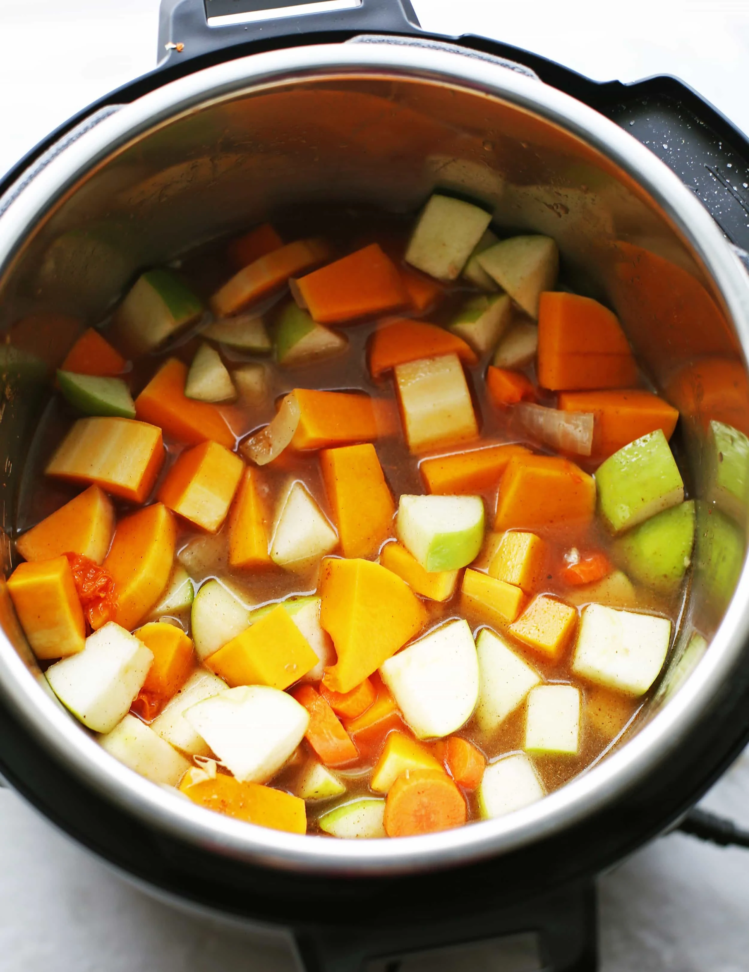 Sautéed onions, ginger, and garlic with chopped butternut squash, granny smith apples, carrots, spices, and vegetable broth are mixed in the Instant Pot.