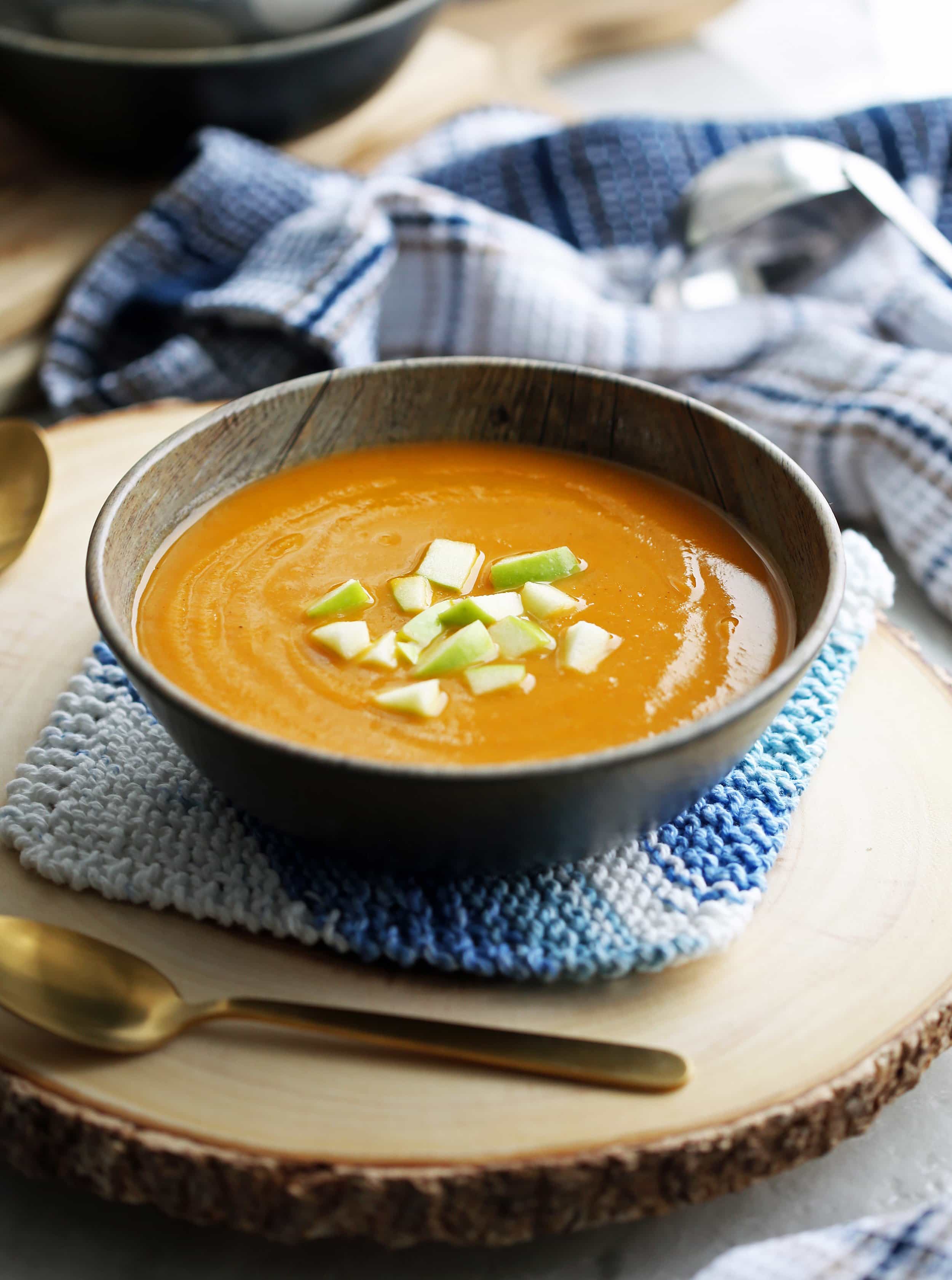 A side view of a bowl of butternut squash apple ginger soup with diced green apples on top.