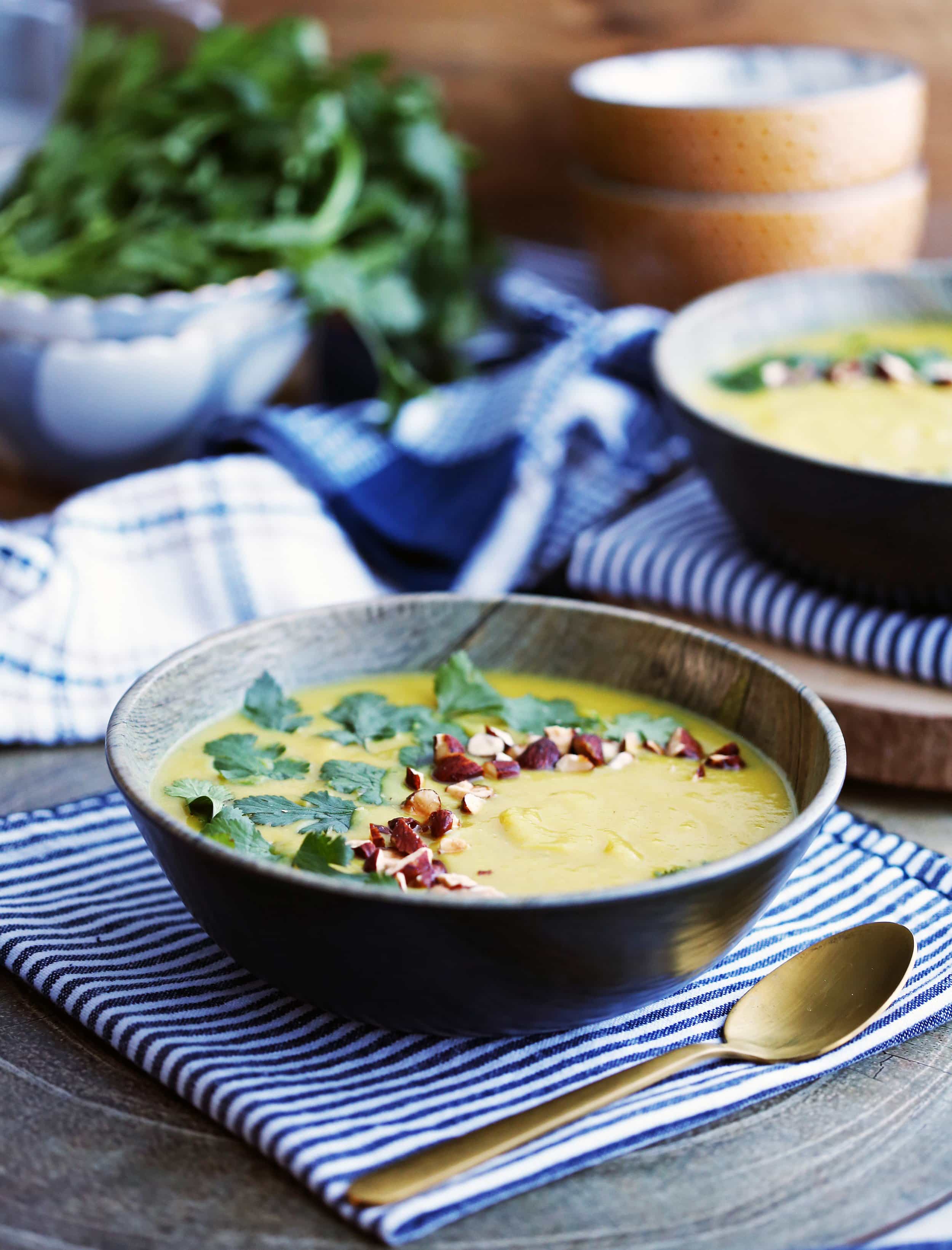 Instant Pot Turmeric Cauliflower Potato Soup topped with cilantro and almonds in a dark-brown bowl with spoon on the side.