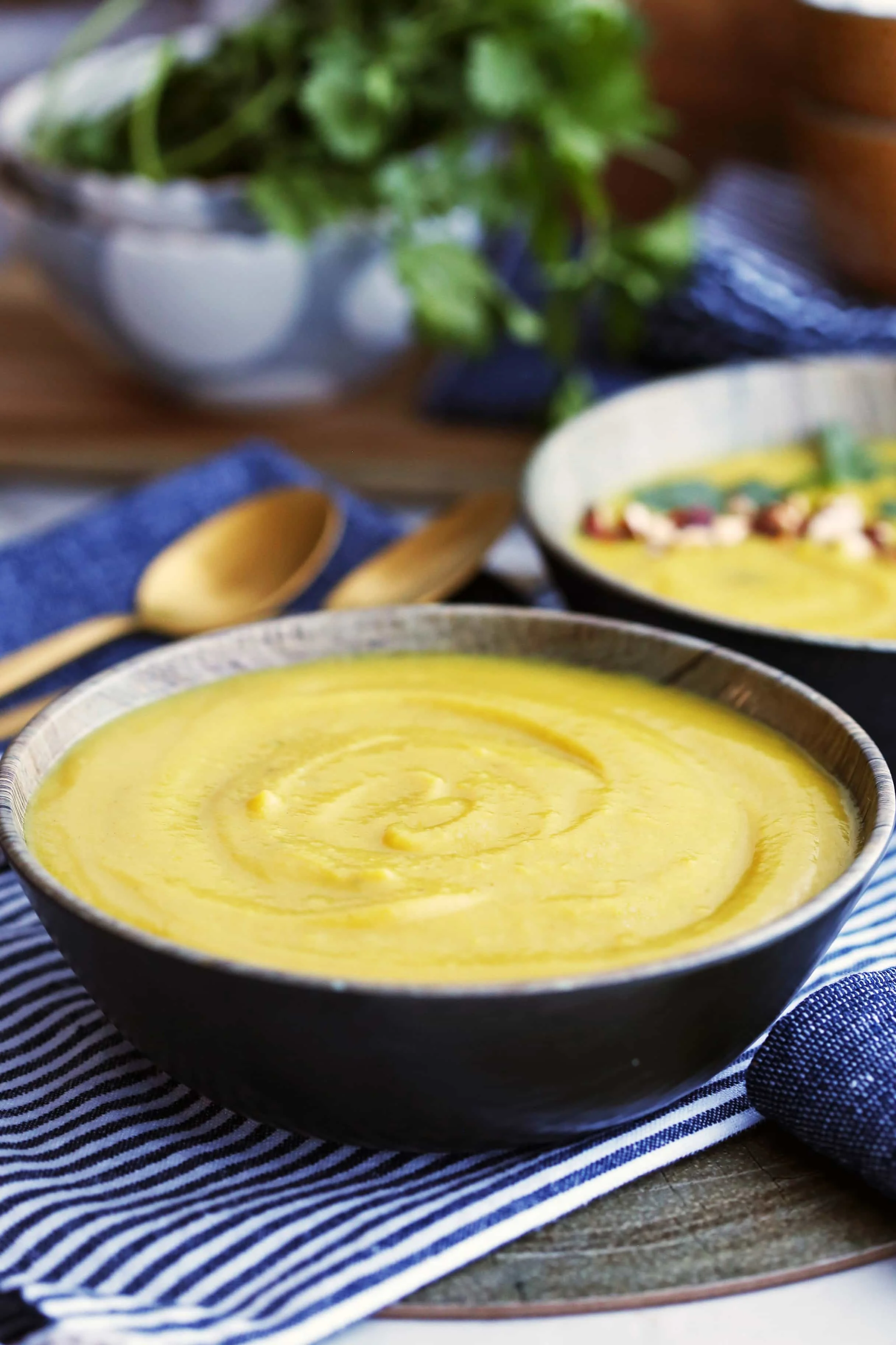 Instant Pot Turmeric Cauliflower Potato Soup in a dark-brown bowl with another bowl of the same soup in the background.