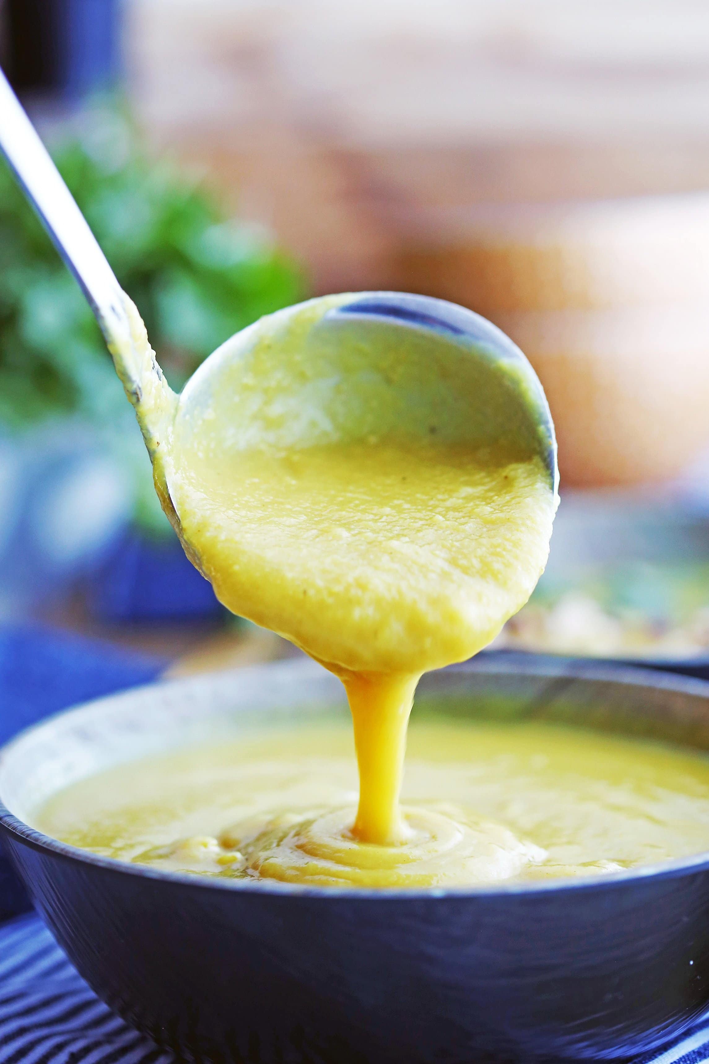 A ladle pouring Instant Pot Turmeric Cauliflower Potato Soup into an almost full bowl of the soup.