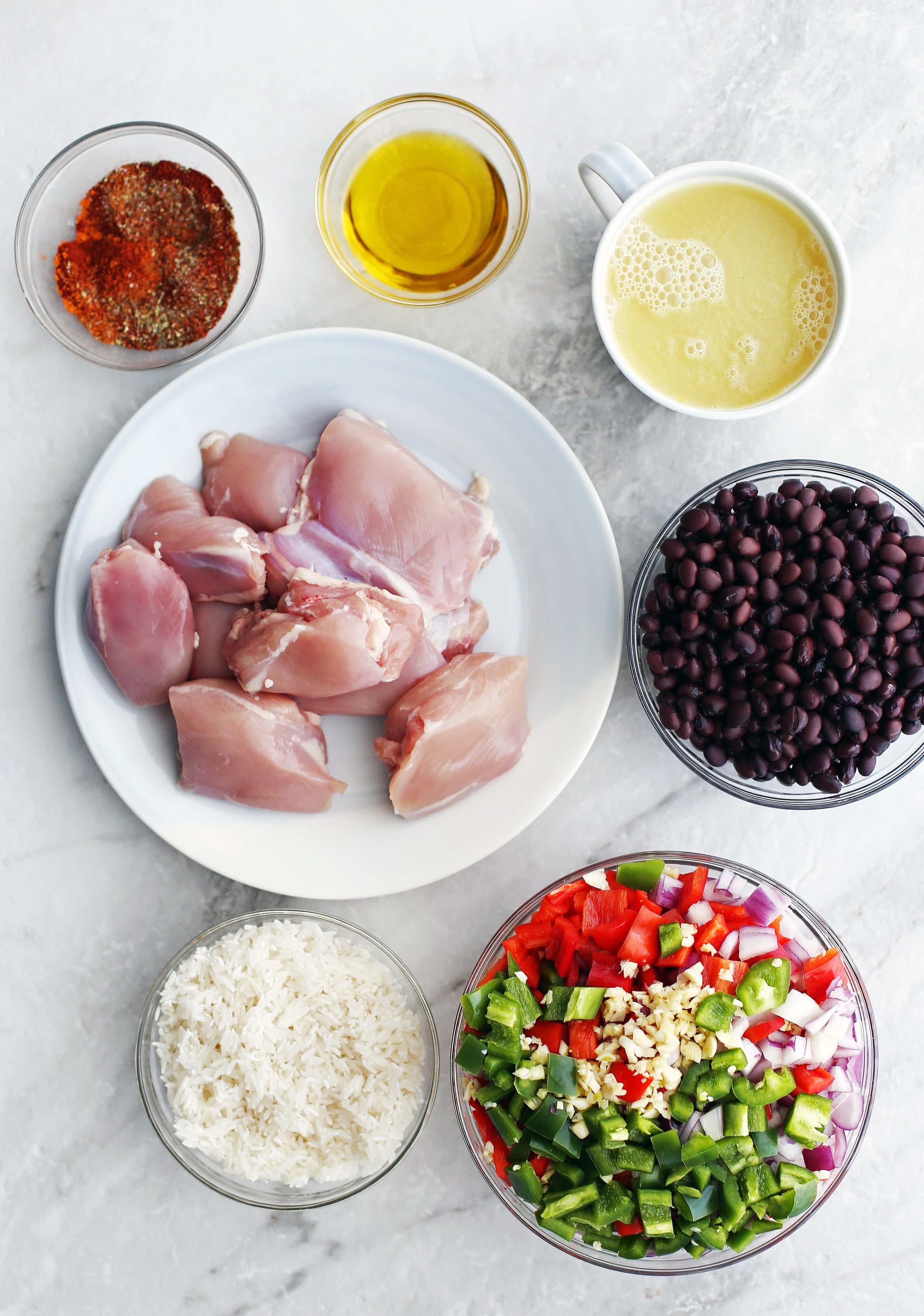 Bowls of chicken thighs, white rice, peppers, onions, black bean, spices, and chicken broth.