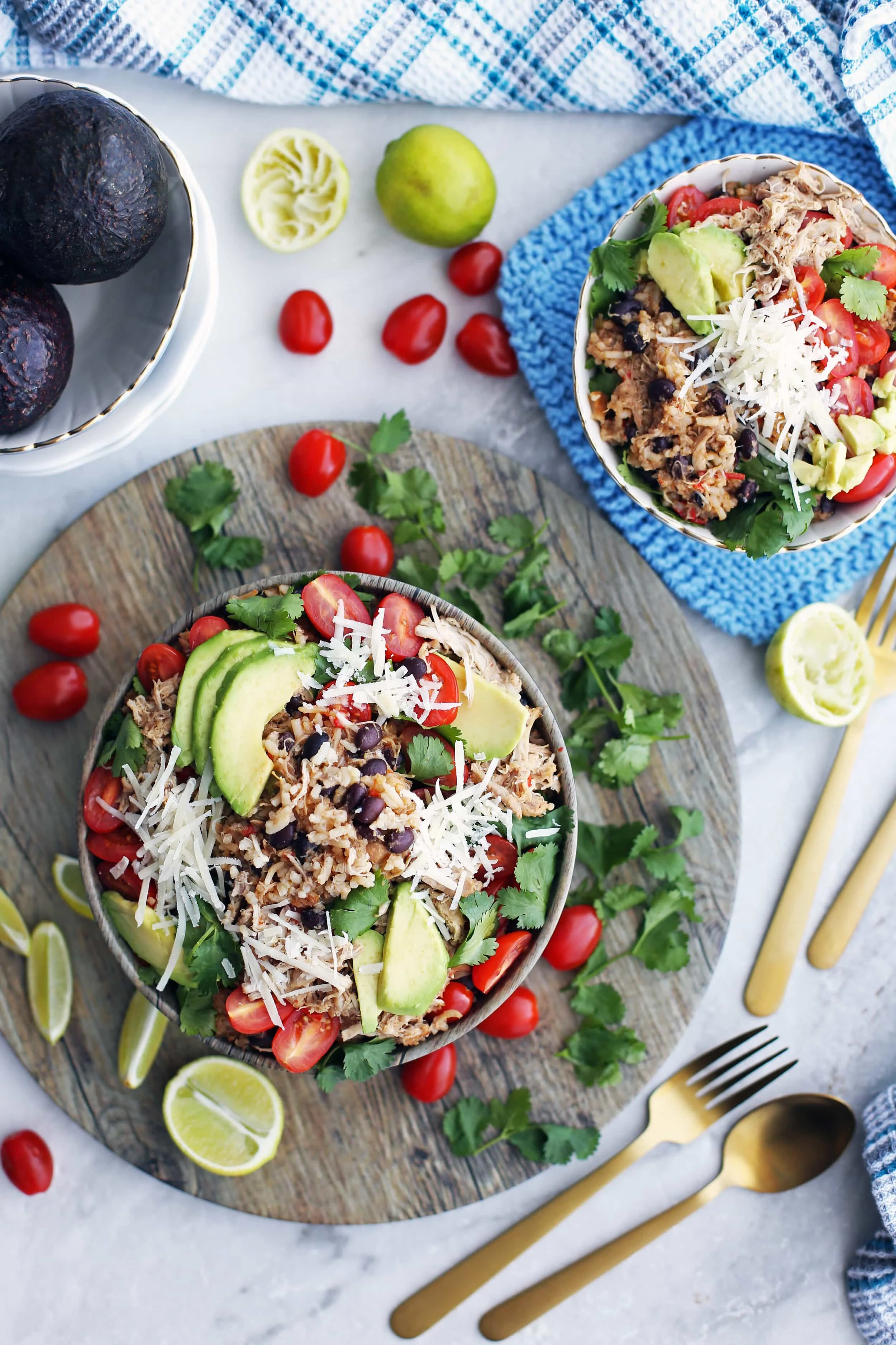 Overhead view of two Instant Pot Chicken and Rice Burrito Bowls topped and surrounded by limes, avocado, tomatoes, cheese, and cilantro.