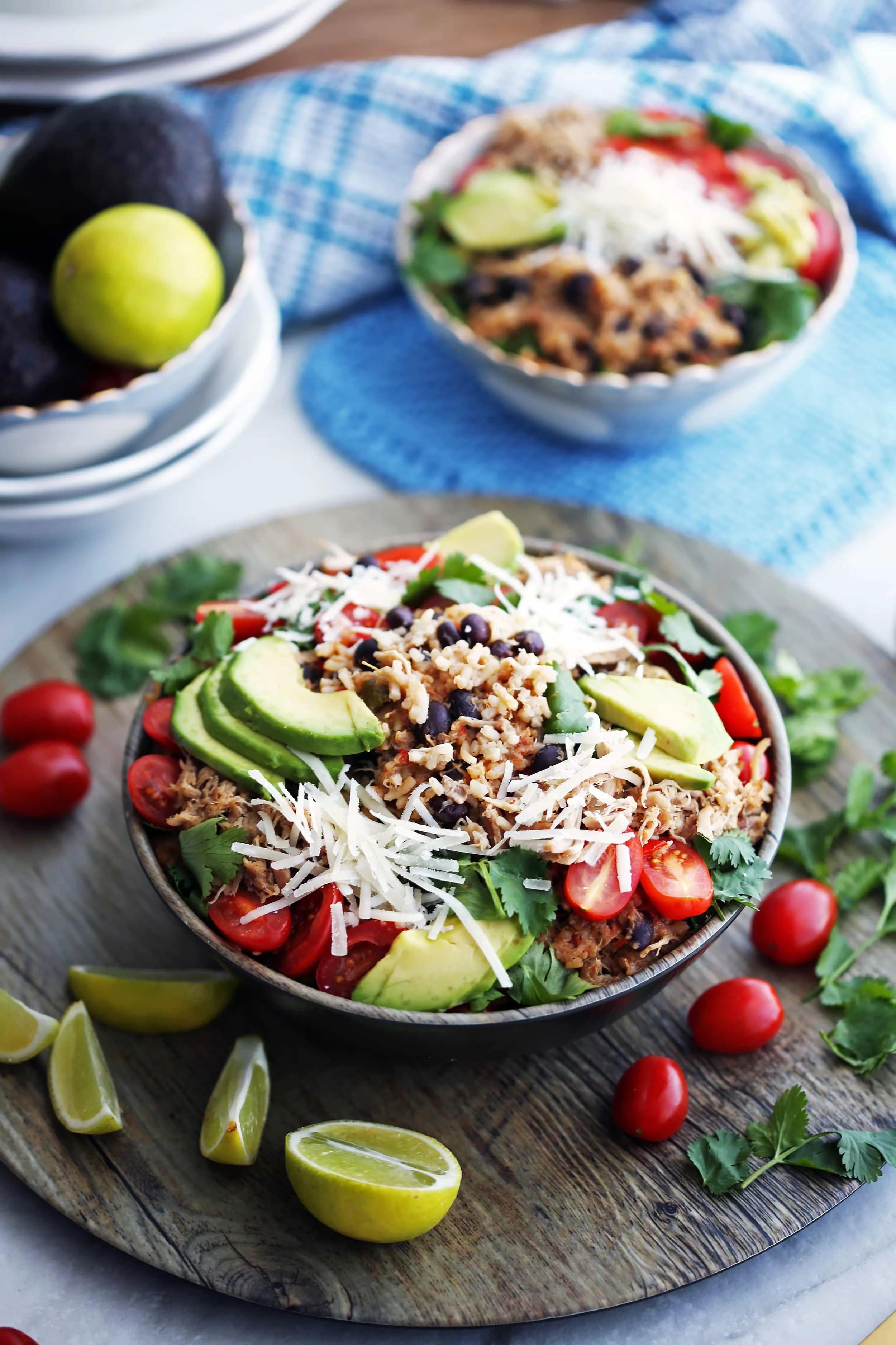 A full bowl of shredded chicken, black beans, and rice that's topped with avocado, cheese, tomatoes, and cilantro.