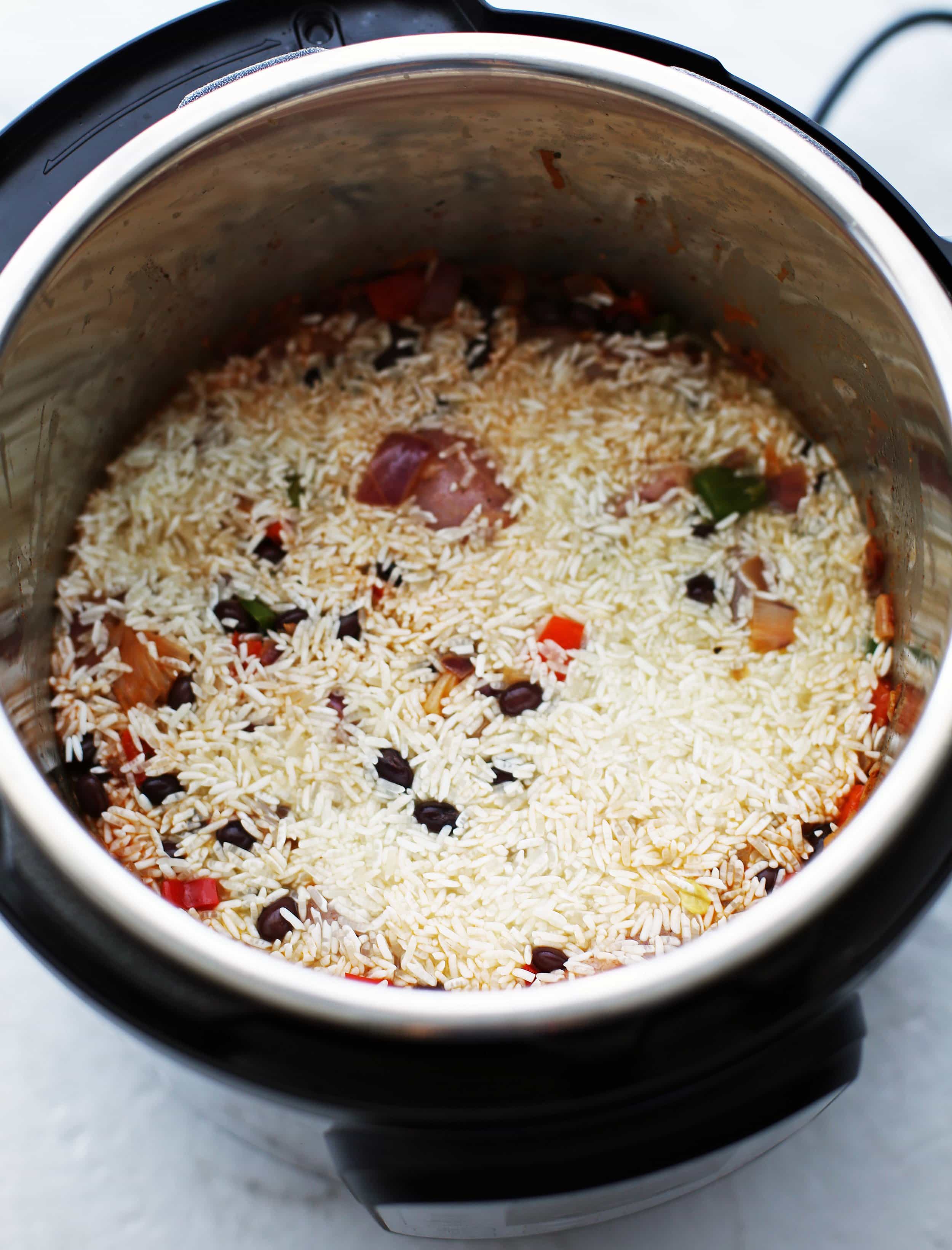 Uncooked white rice on top of sauteed vegetables, black beans, and raw chicken thighs in the Instant Pot.