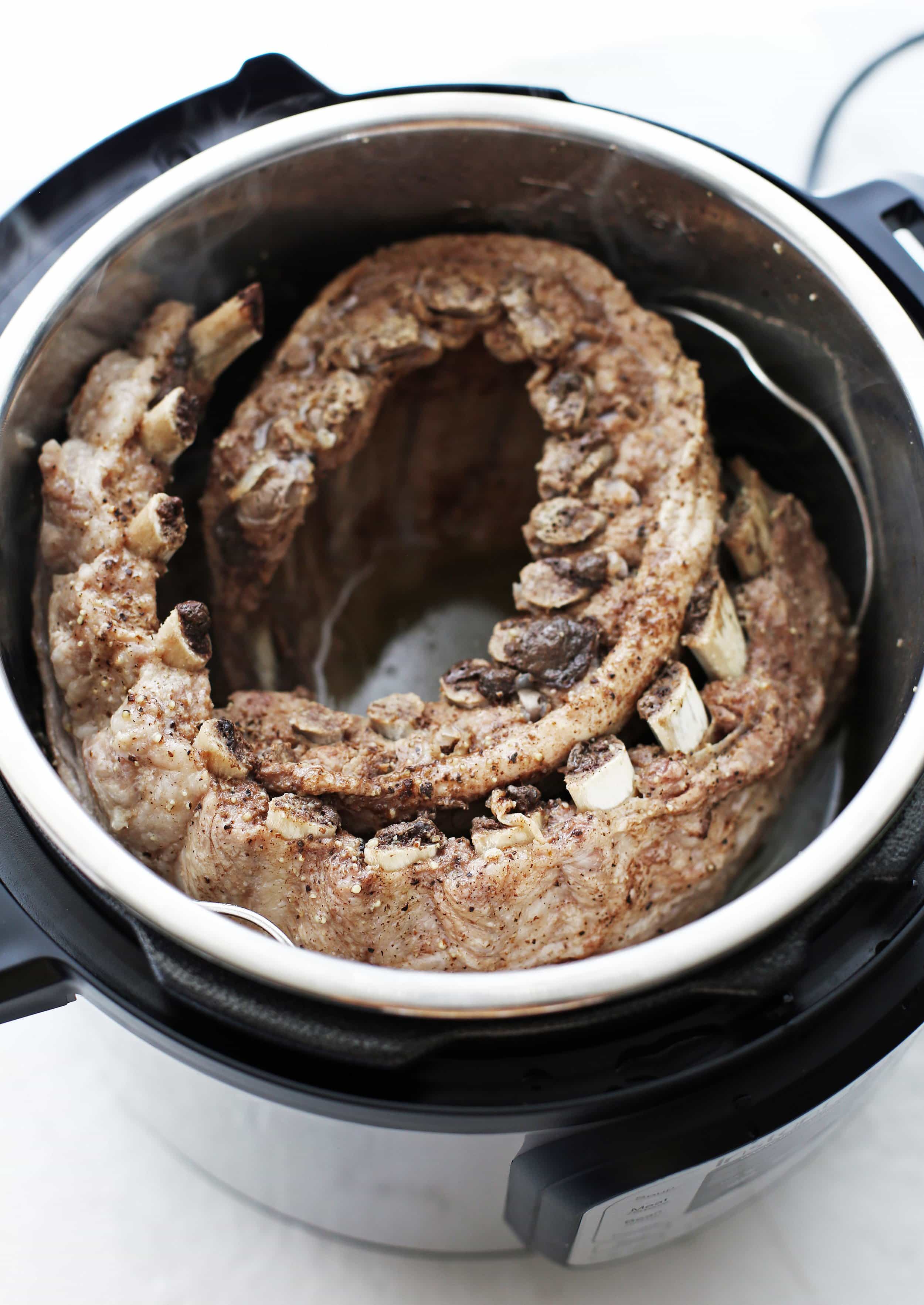 Two cooked rack of pork ribs curled around the inside of an Instant Pot.