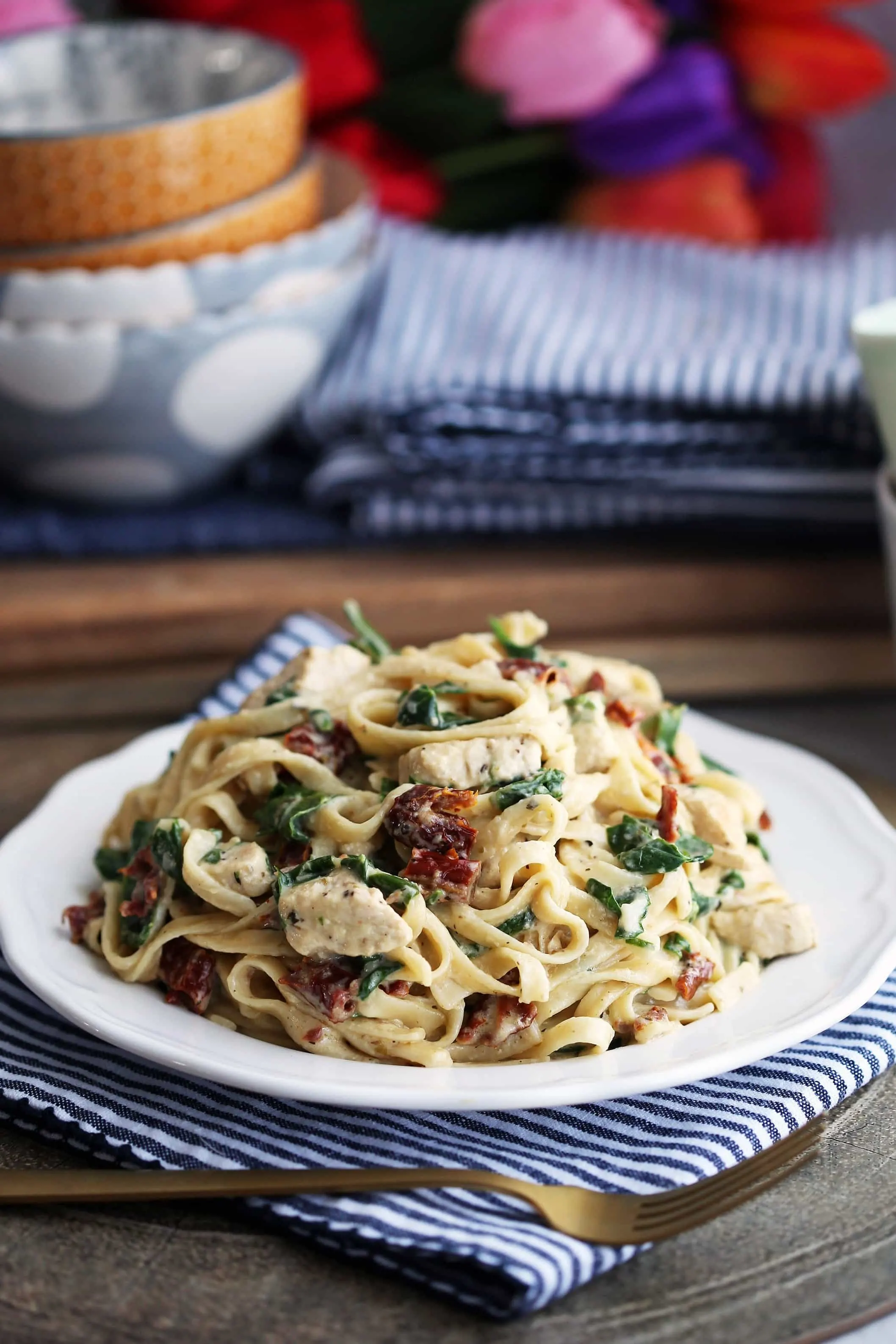Instant Pot creamy fettuccine with chicken, spinach, and sun-dried tomatoes on a white plate.