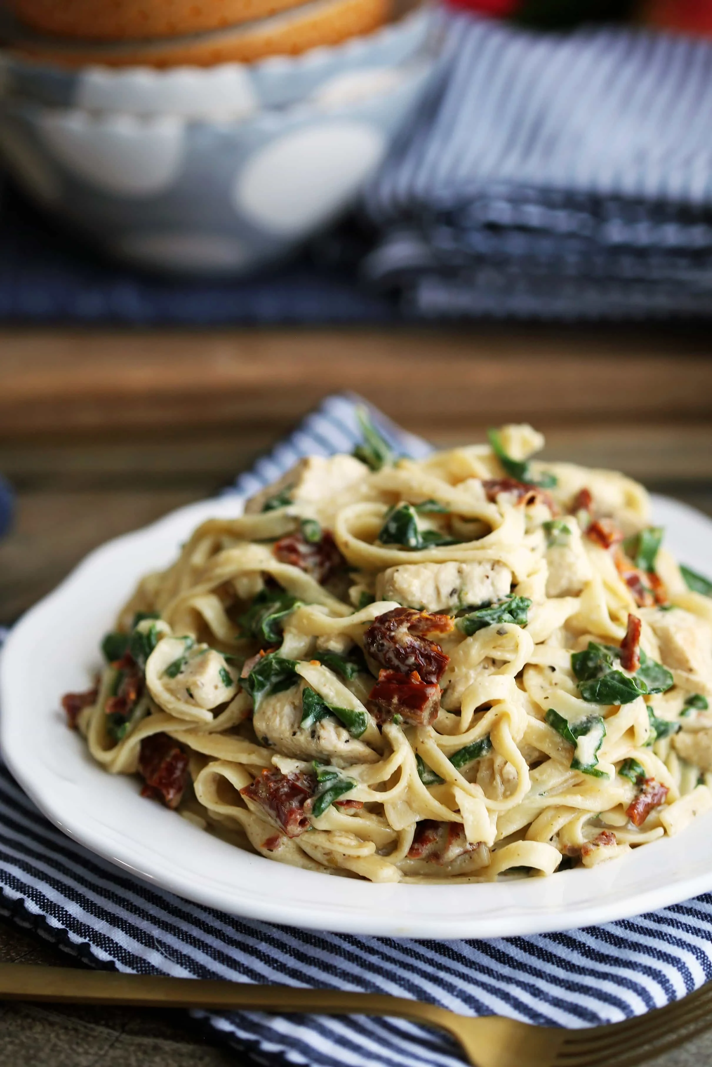 Instant Pot pasta with cream sauce, chicken, baby spinach, and sun-dried tomatoes on a white plate.