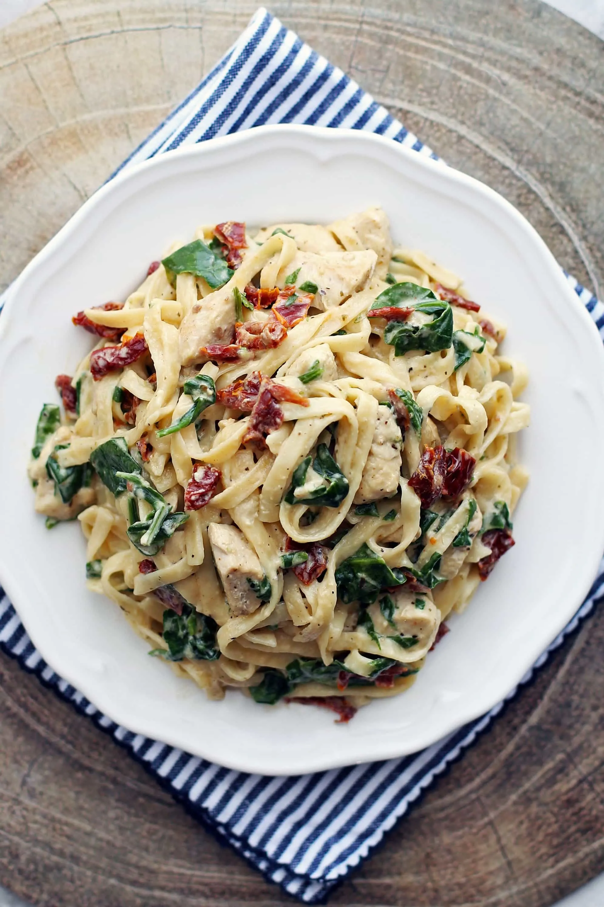 An overhead view of Instant Pot creamy fettuccine with chicken, baby spinach, and sun-dried tomatoes on a white plate.
