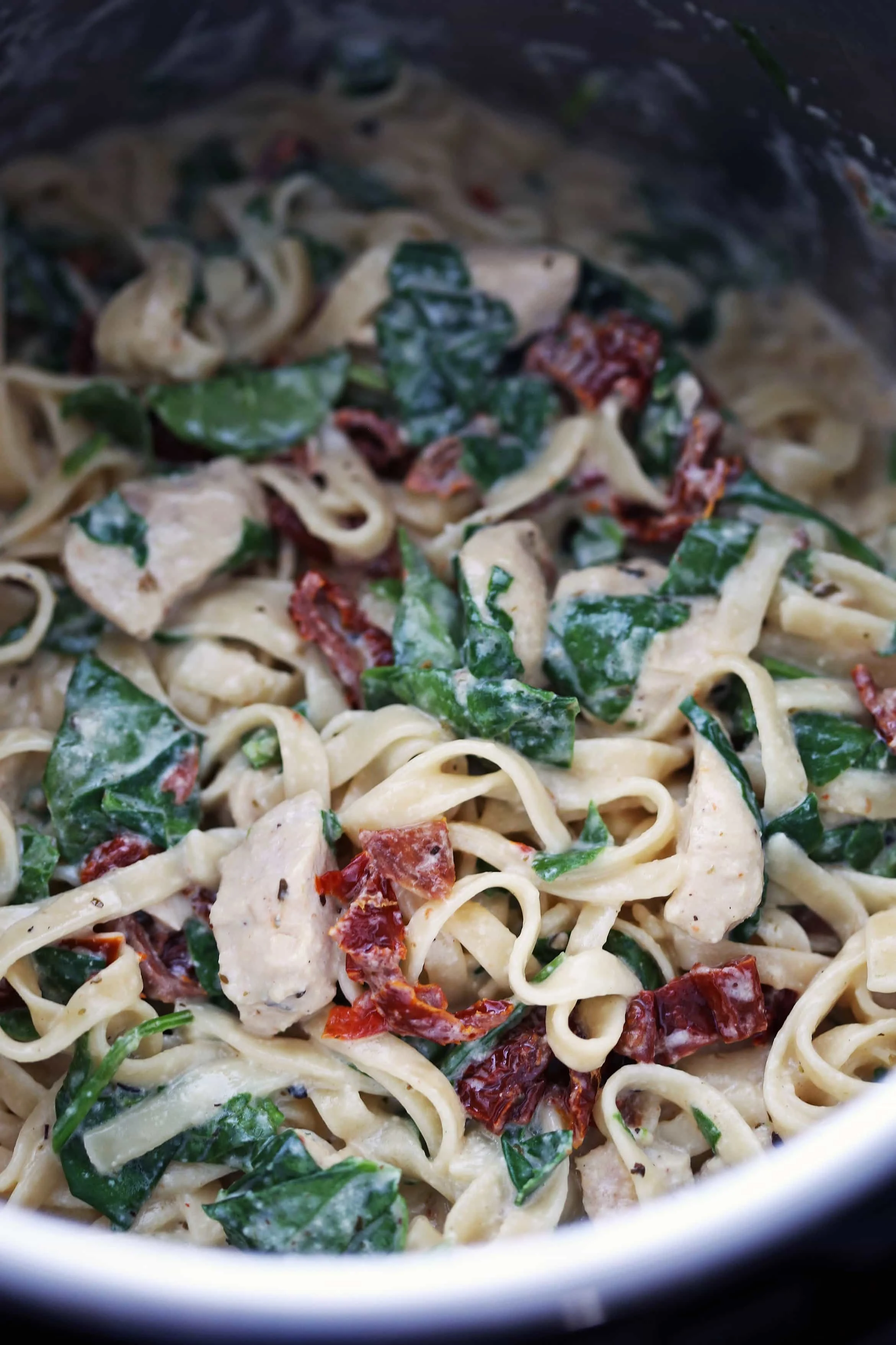 Creamy fettuccine pasta tossed in a creamy sauce with chicken, sun-dried tomatoes, and baby spinach in the Instant Pot.