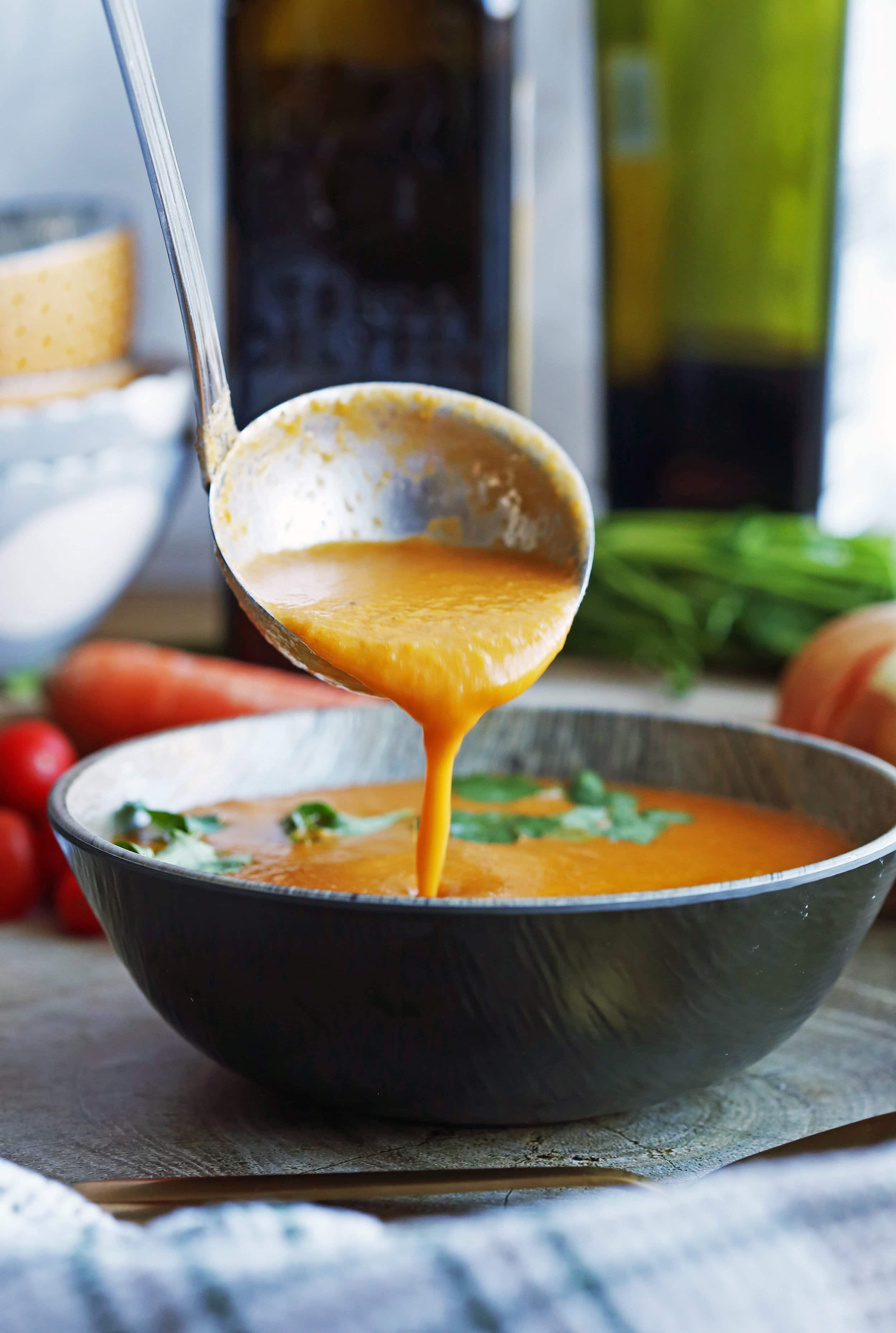 Tomato soup being poured using a metal ladle into a wooden bowl.