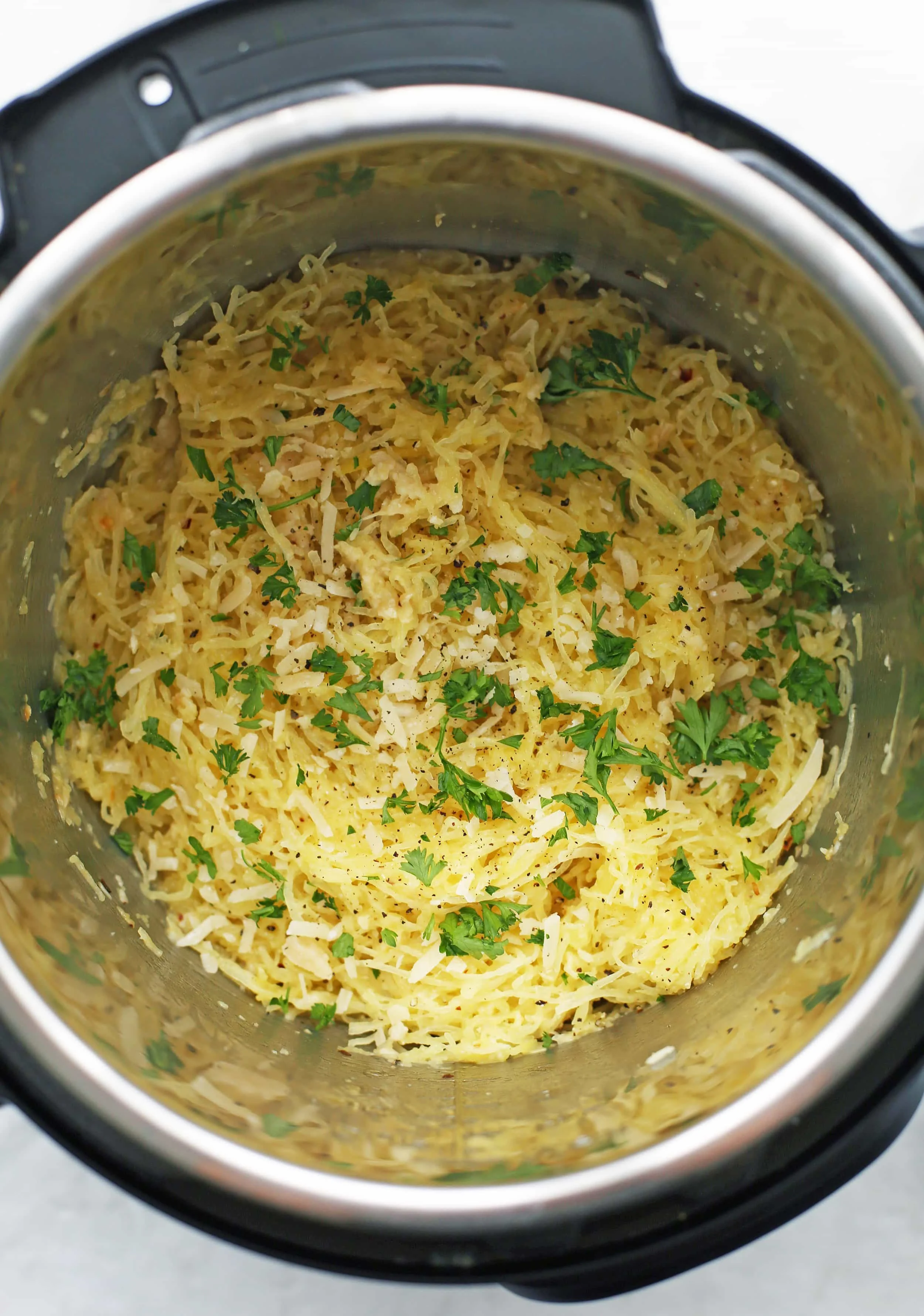 Cooked spaghetti squash mixed with olive oil, butter, spices, garlic, parmesan, and parsley in the Instant Pot.