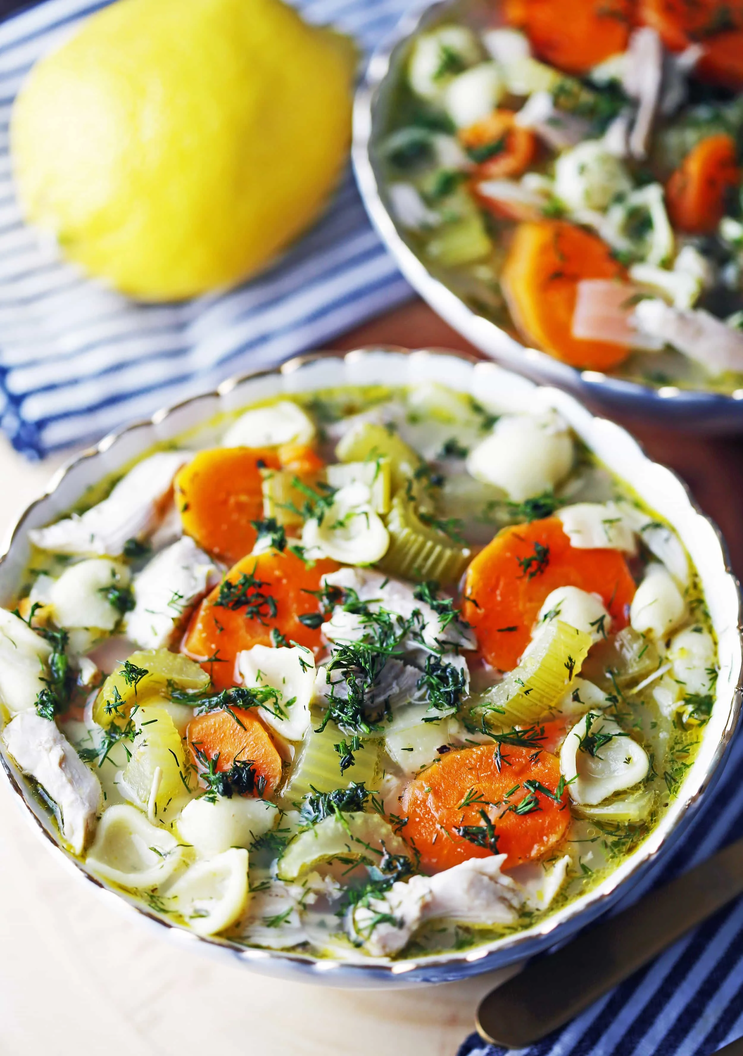 A full bowl of Lemon Dill Chicken Noodle Soup on a wooden board.