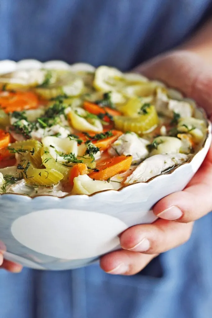 Hands holding a blue and white bowl that’s full of Lemon Dill Chicken Noodle Soup.