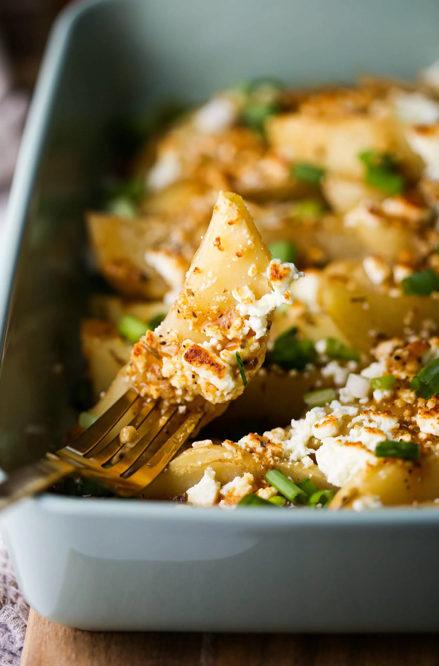 A close-up of a lemon feta potato wedge pieced on a fork.