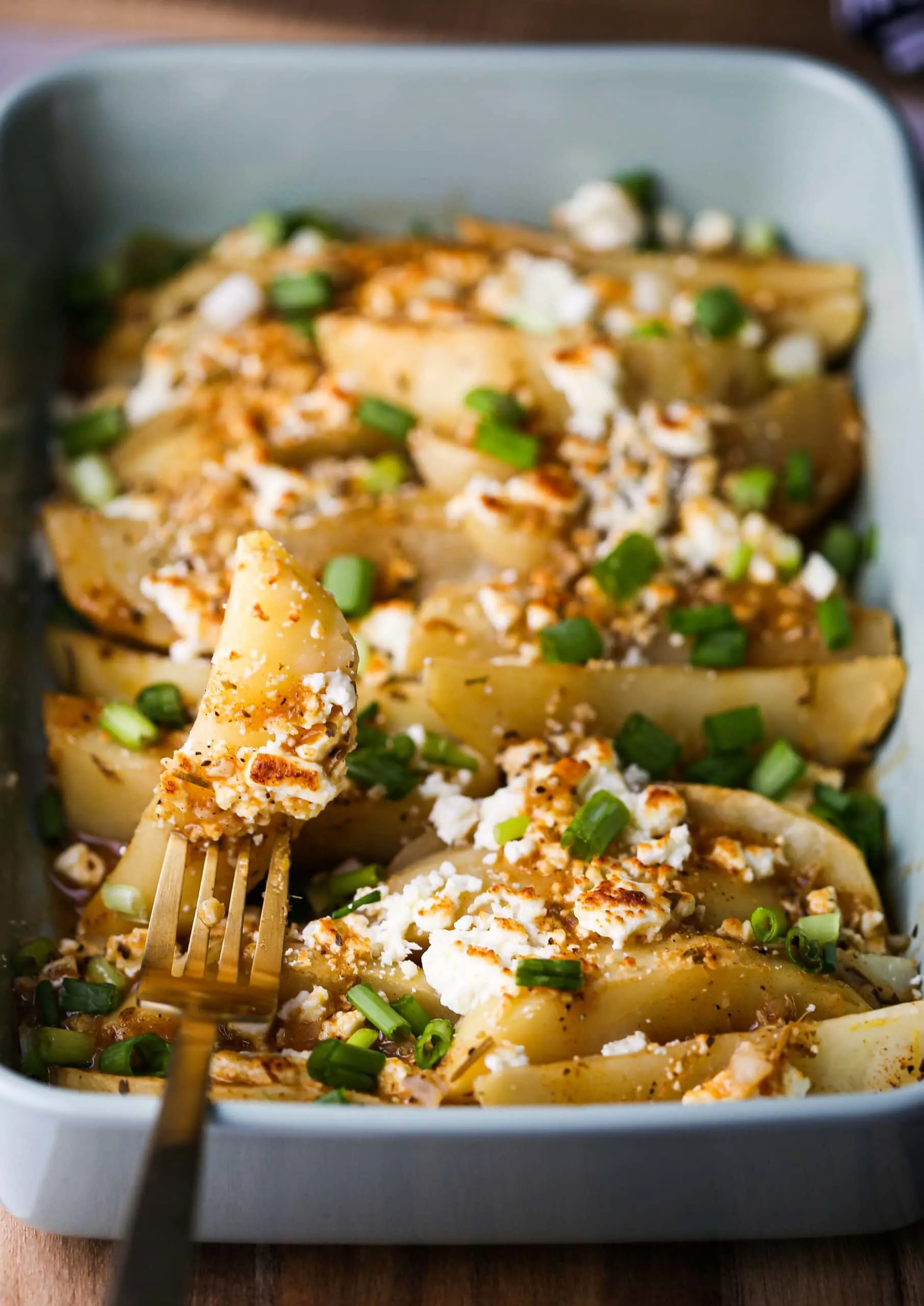 Lemon feta potato wedges in a green casserole dish and a wedge on a fork too.