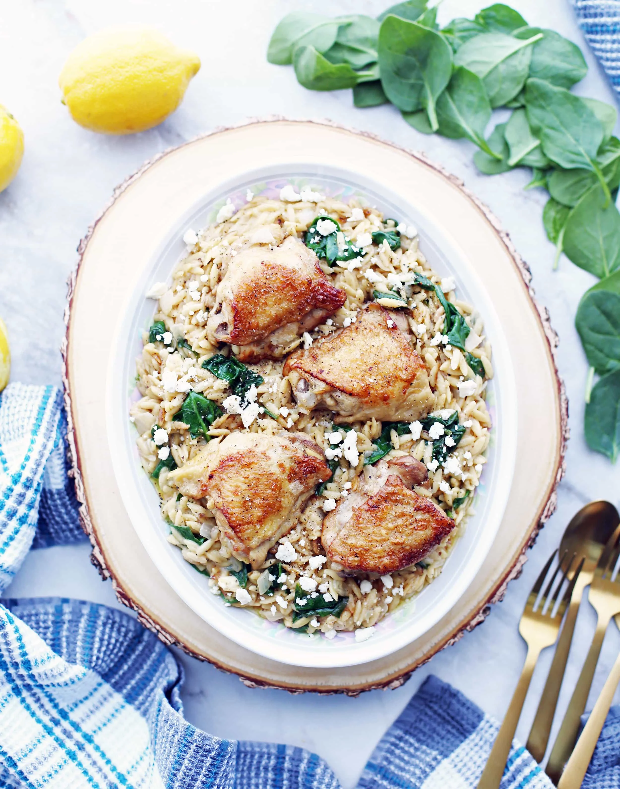 Cooked chicken thighs placed on top of lemon pepper orzo with feta and spinach on a large oval platter.