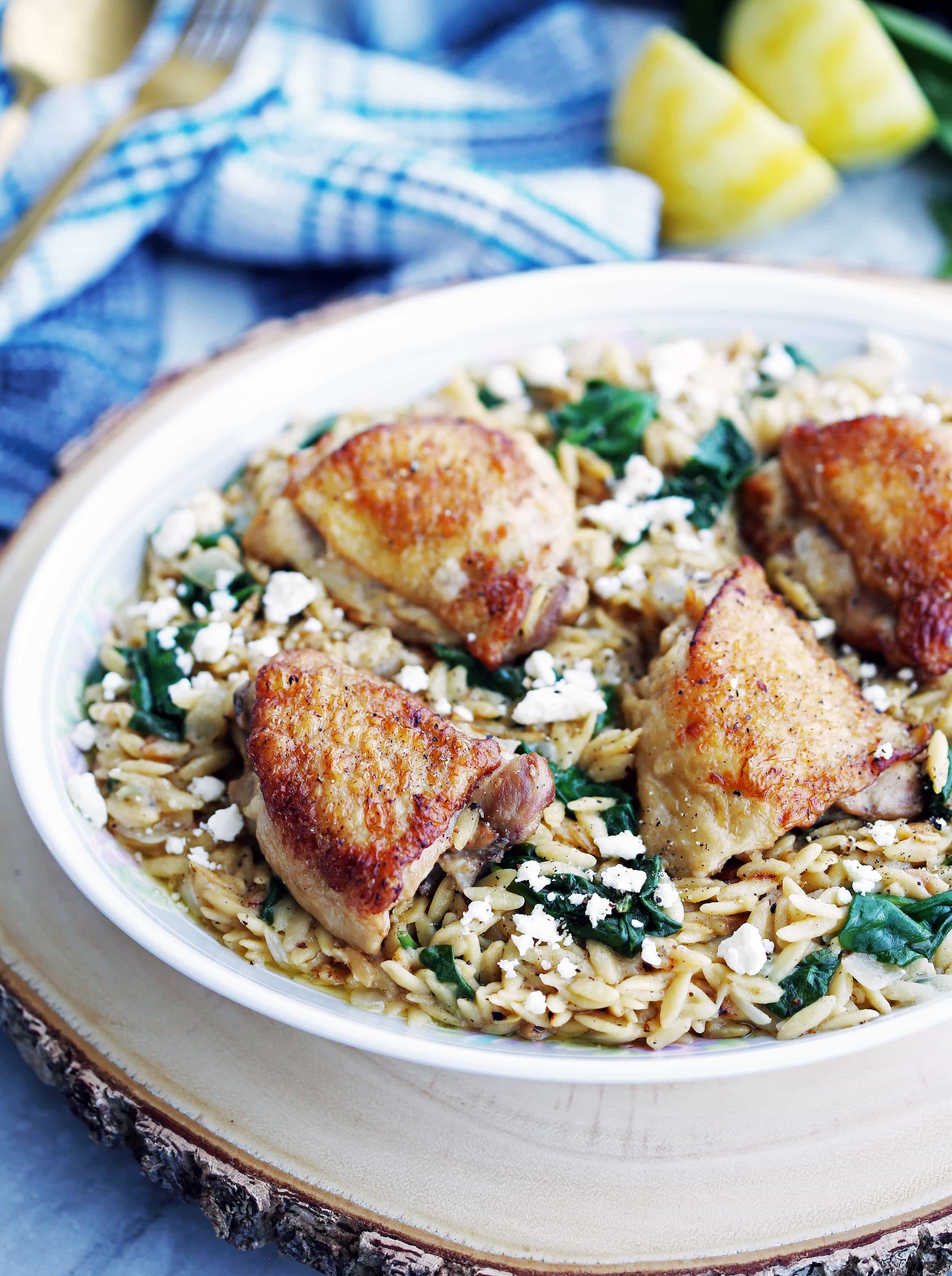Crispy skin chicken thighs and lemon pepper orzo with feta and spinach on a large oval platter.