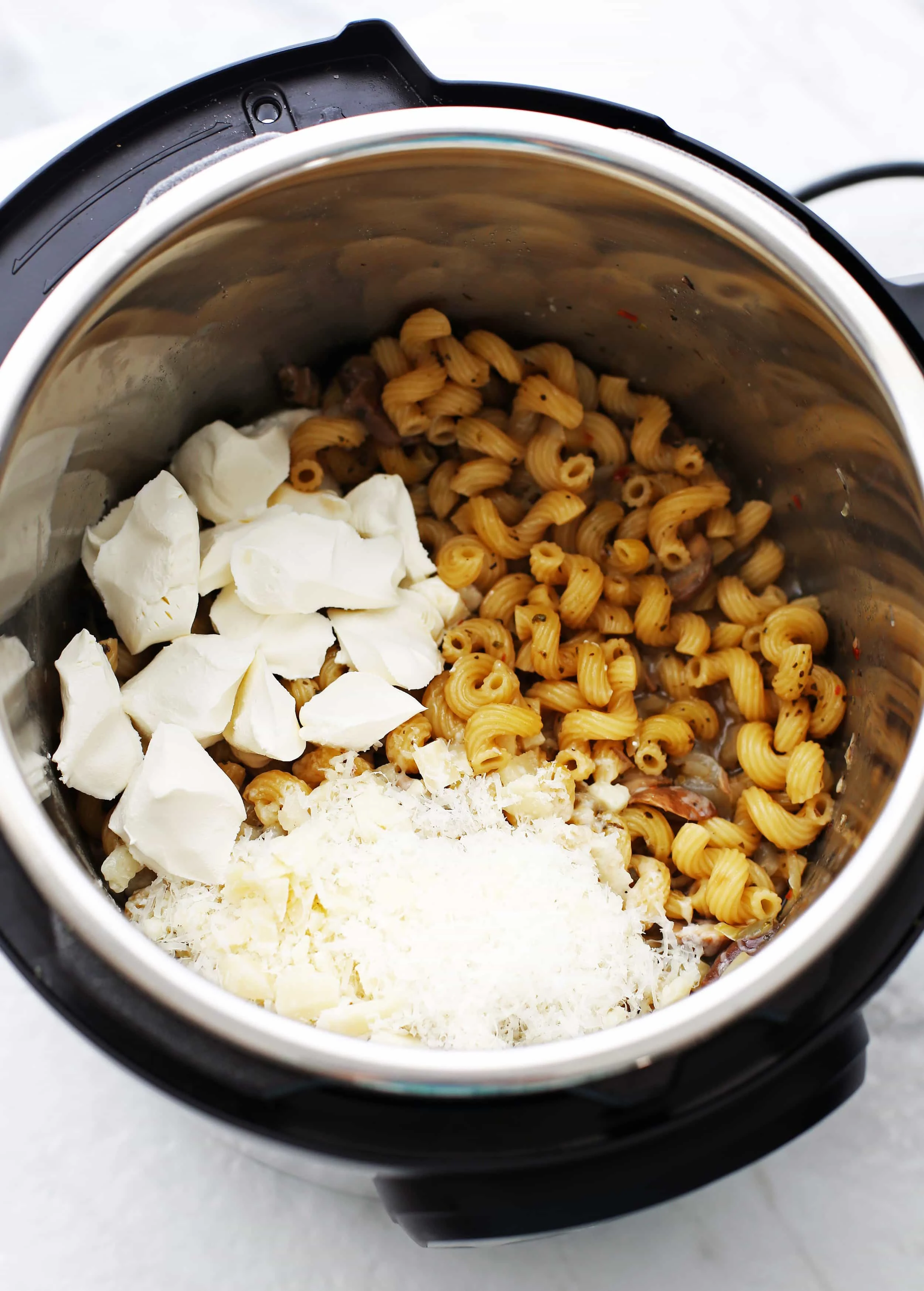 Cooked cavatappi pasta with cream cheese and grated parmesan on top in an Instant Pot.