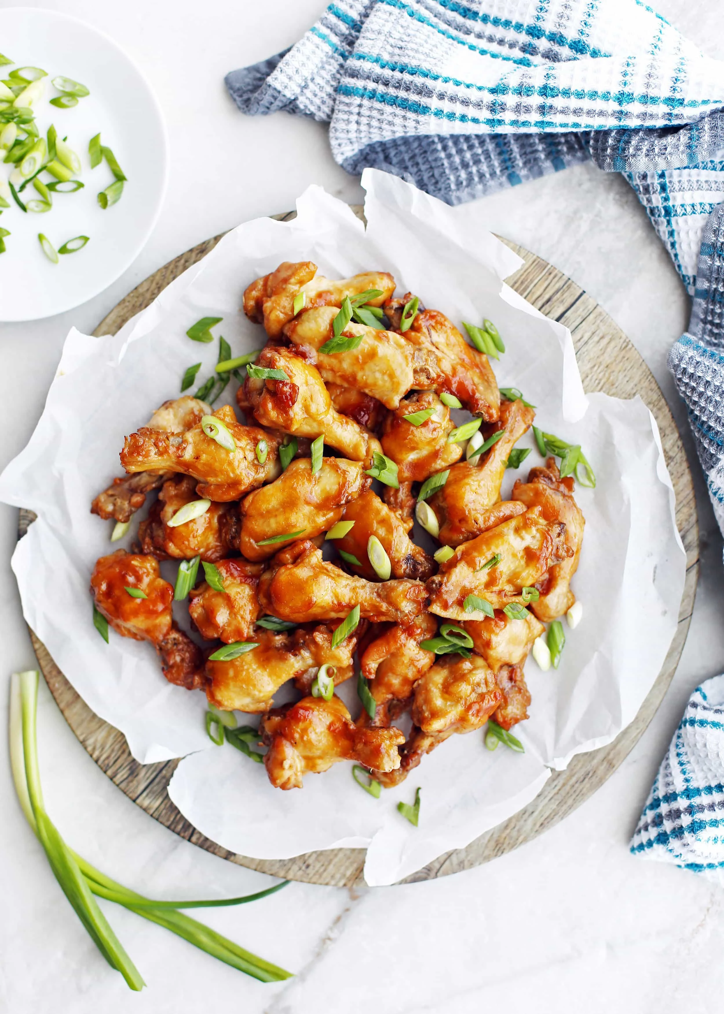 Overhead view of Instant Pot Orange Teriyaki Chicken Wings piled on a parchment paper-topped wooden platter.