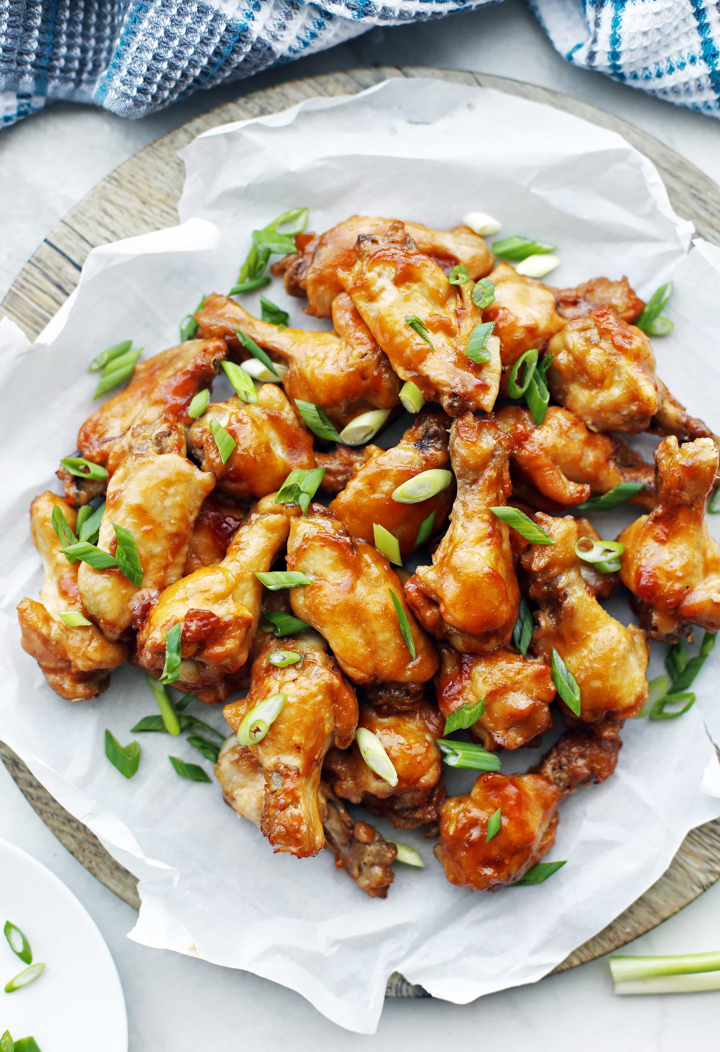 Overhead view of Instant Pot Orange Teriyaki Chicken Wings topped with green onions and piled on a large wooden platter.