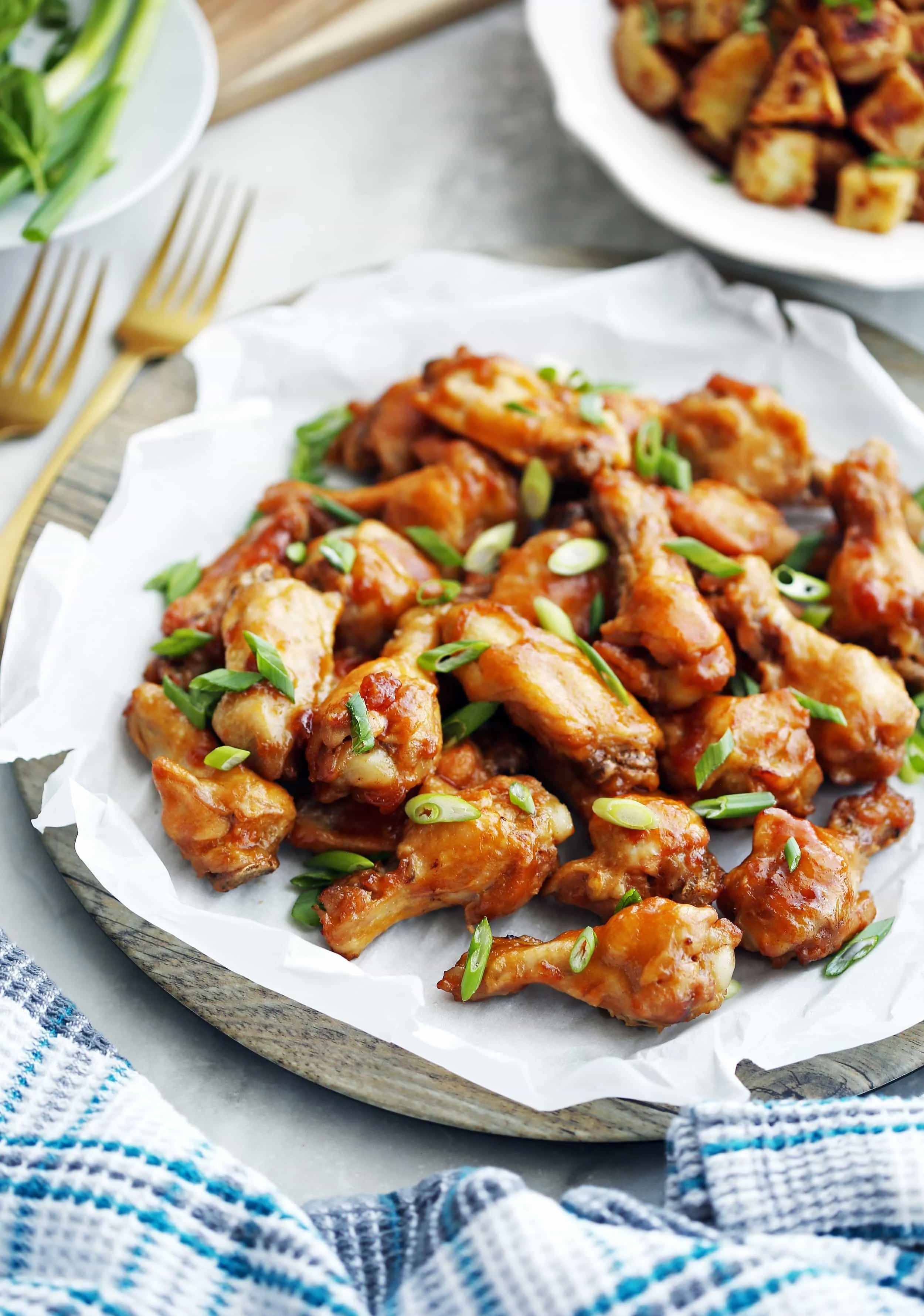 A large wooden platter full of Instant Pot Orange Teriyaki Chicken Wings with green onions on top.