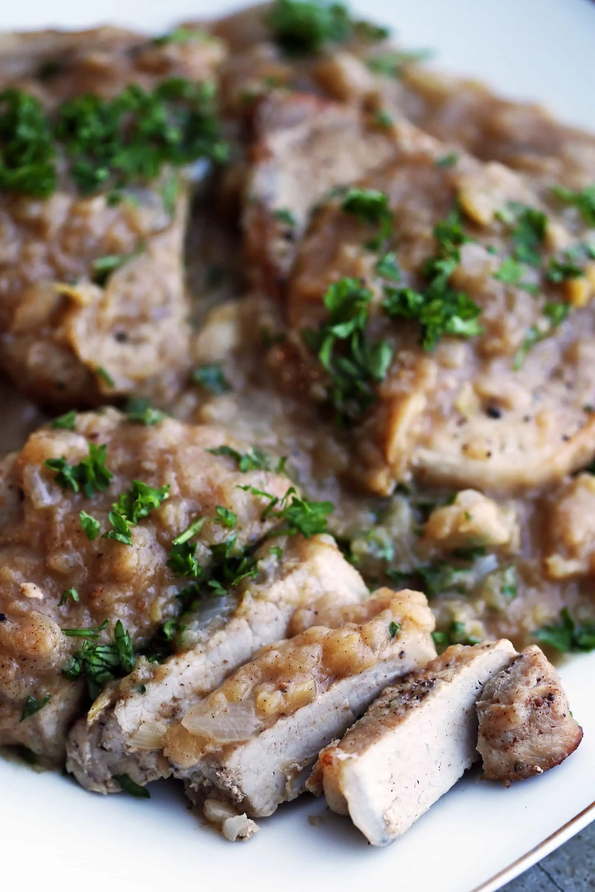 A closeup of a sliced boneless pork chop covered with onion-apple sauce and garnished with fresh parsley.